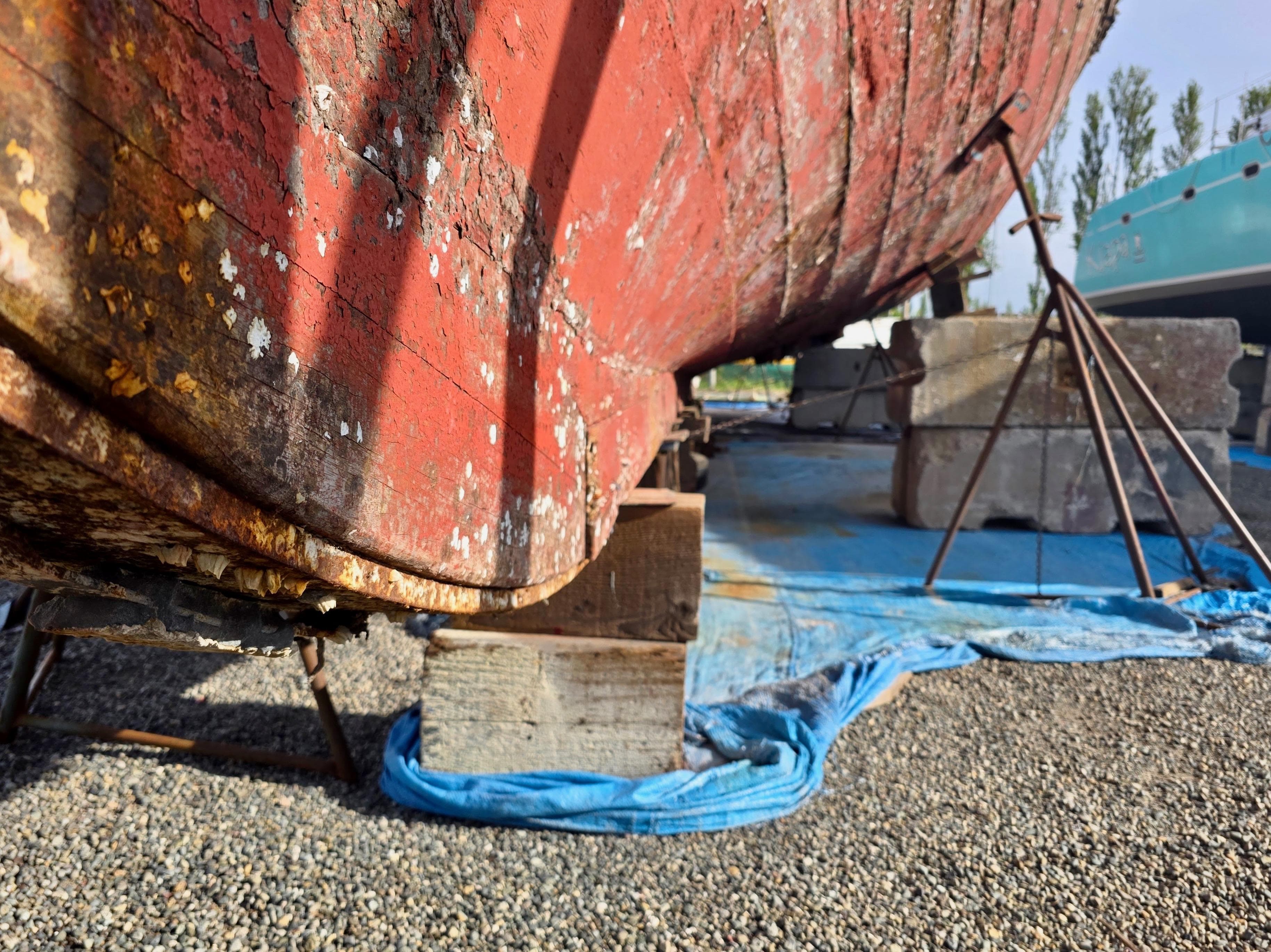 Historic 1890 custom tugboat on dry dock, weathered red hull, supported by blocks and tarp.