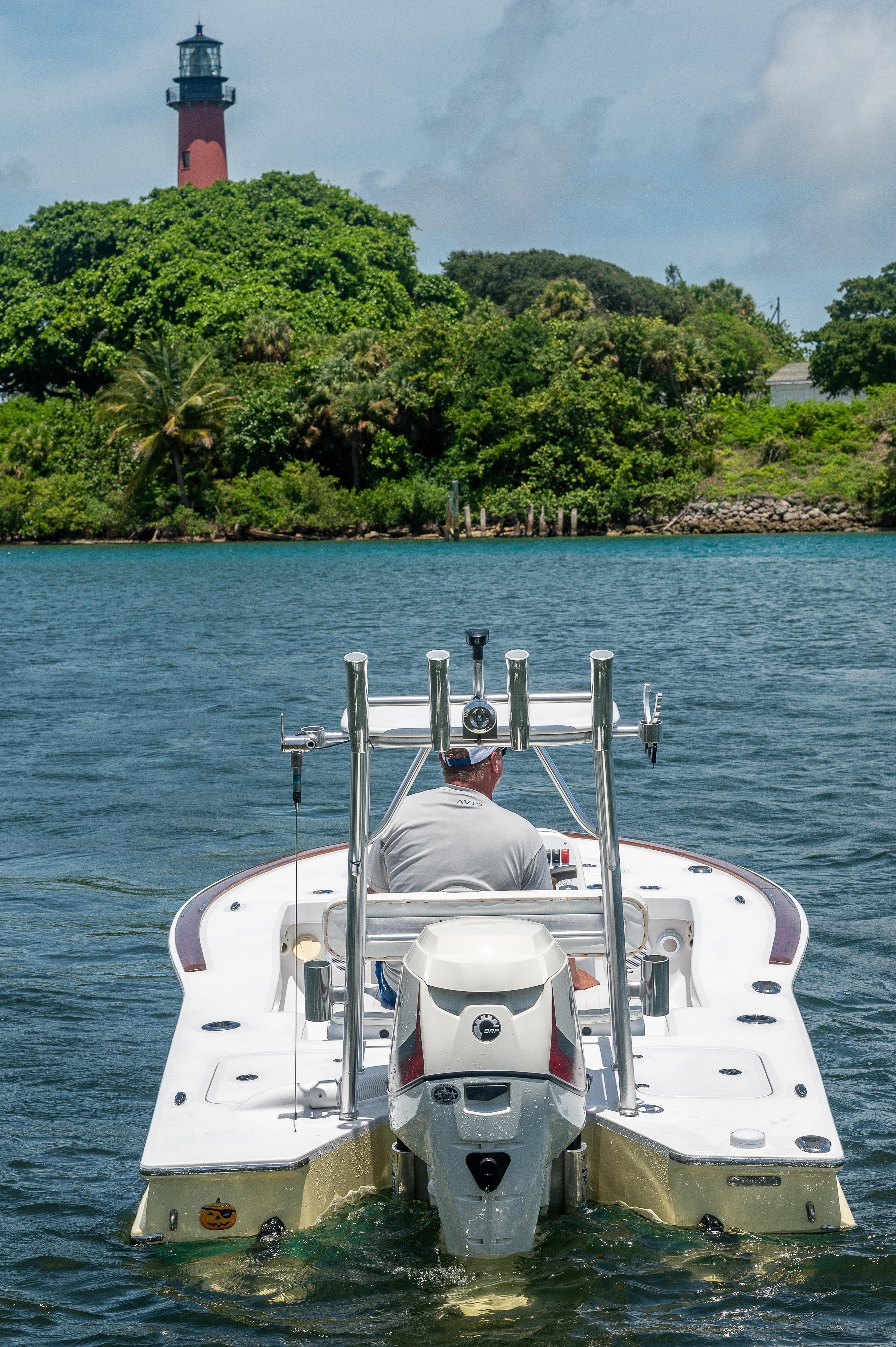 Man driving 2017 Custom Envi Redfisher boat near a lighthouse on a sunny day.