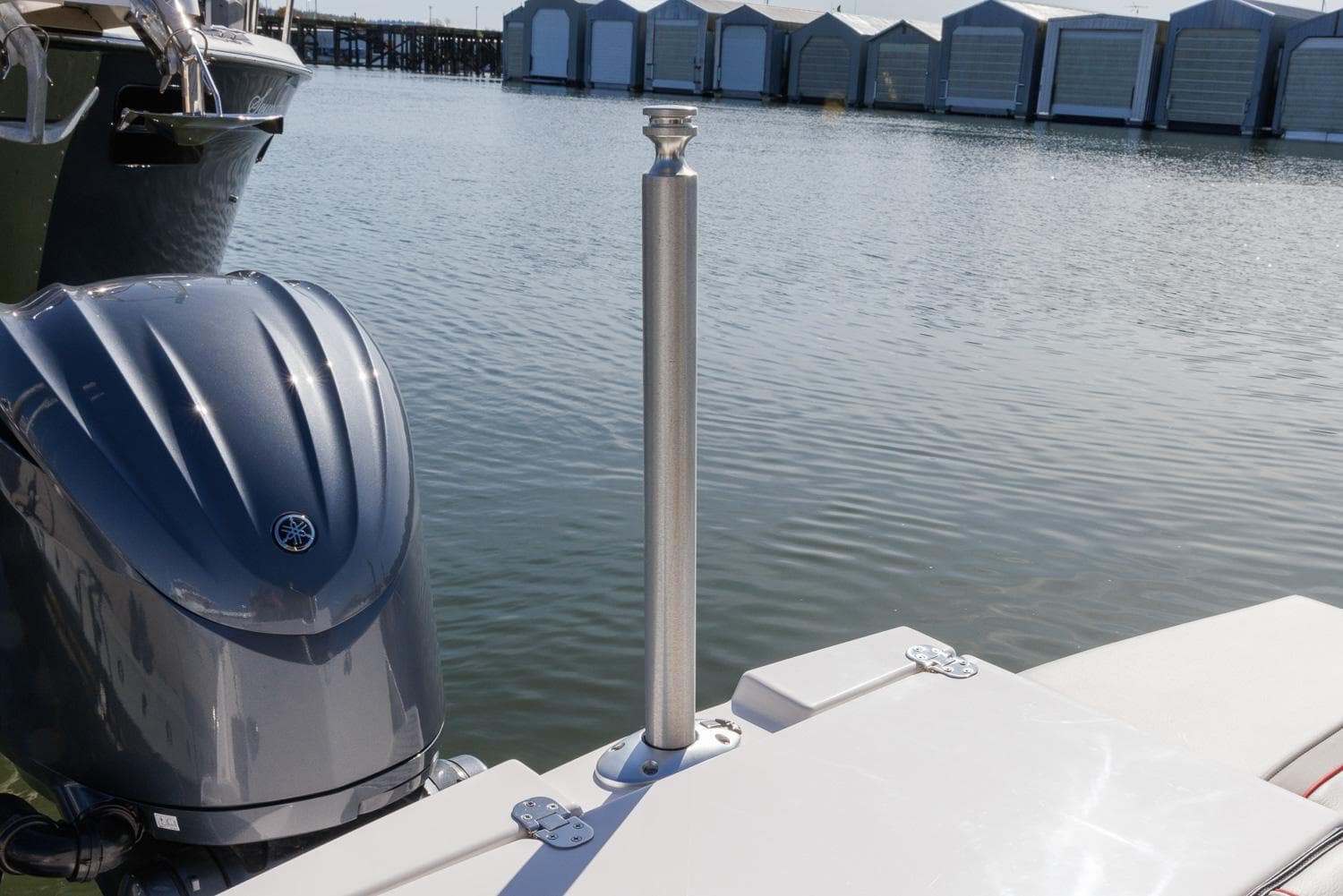 Boat docked by water with outboard motor and metal post, near storage units.