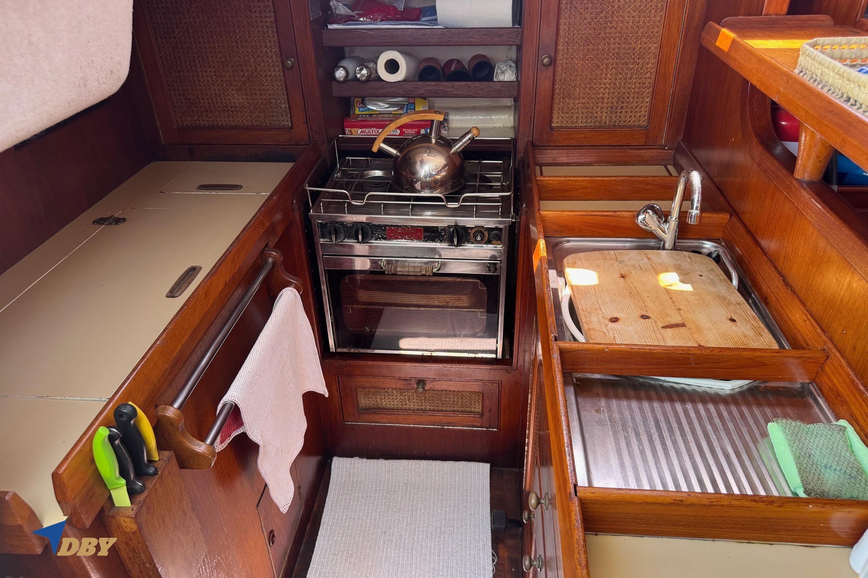 Compact kitchen in a 1987 Bowman 47 yacht with stove, sink, and wooden cabinetry.