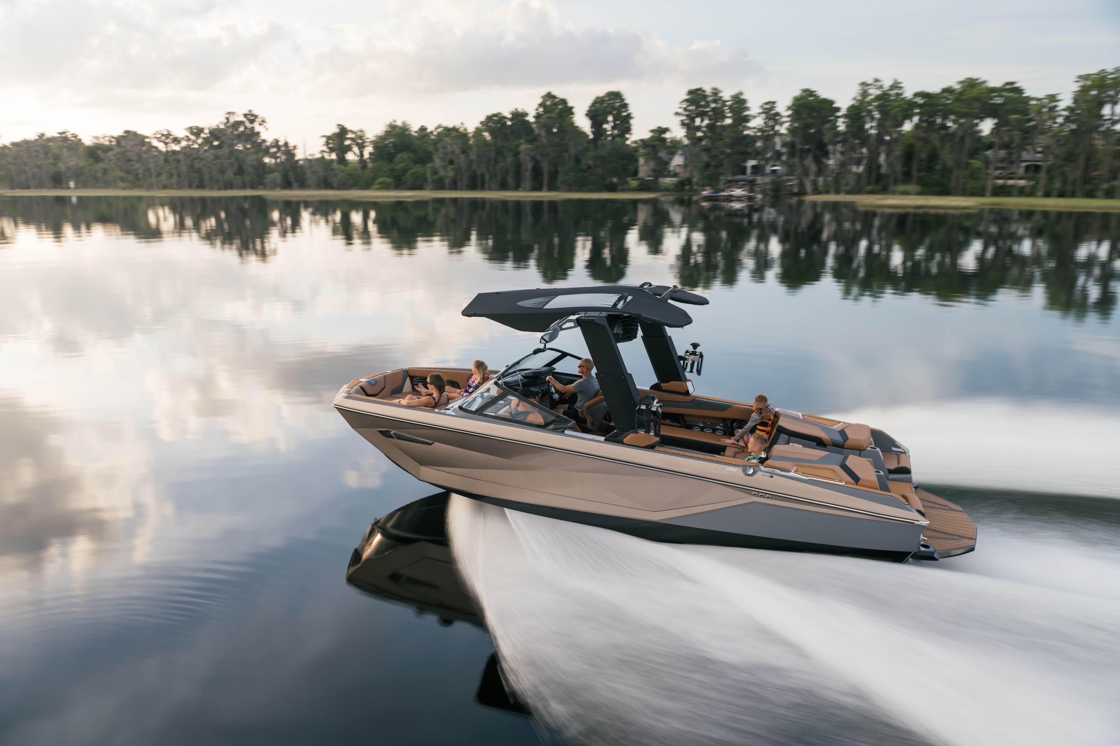 Nautique G25 MY2026 boat cruising on a serene lake with a forested backdrop.
