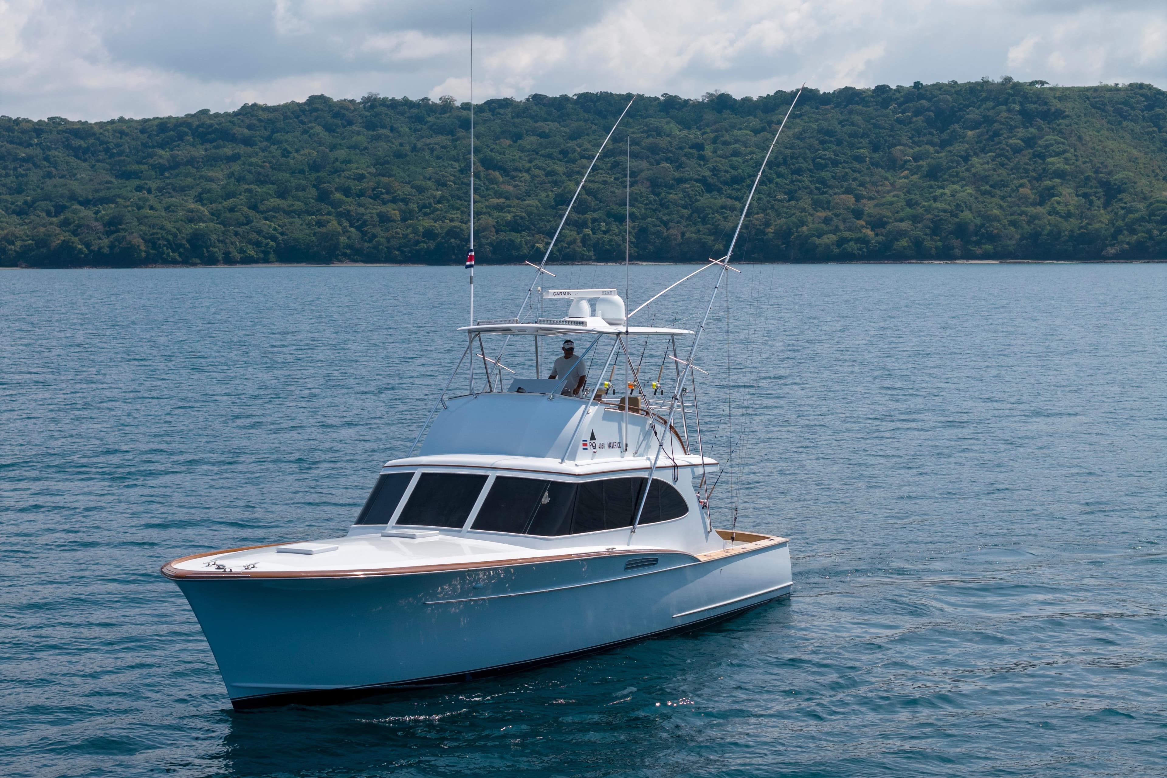 1972 Rybovich Convertible yacht cruising on serene waters with lush green hills in the background.