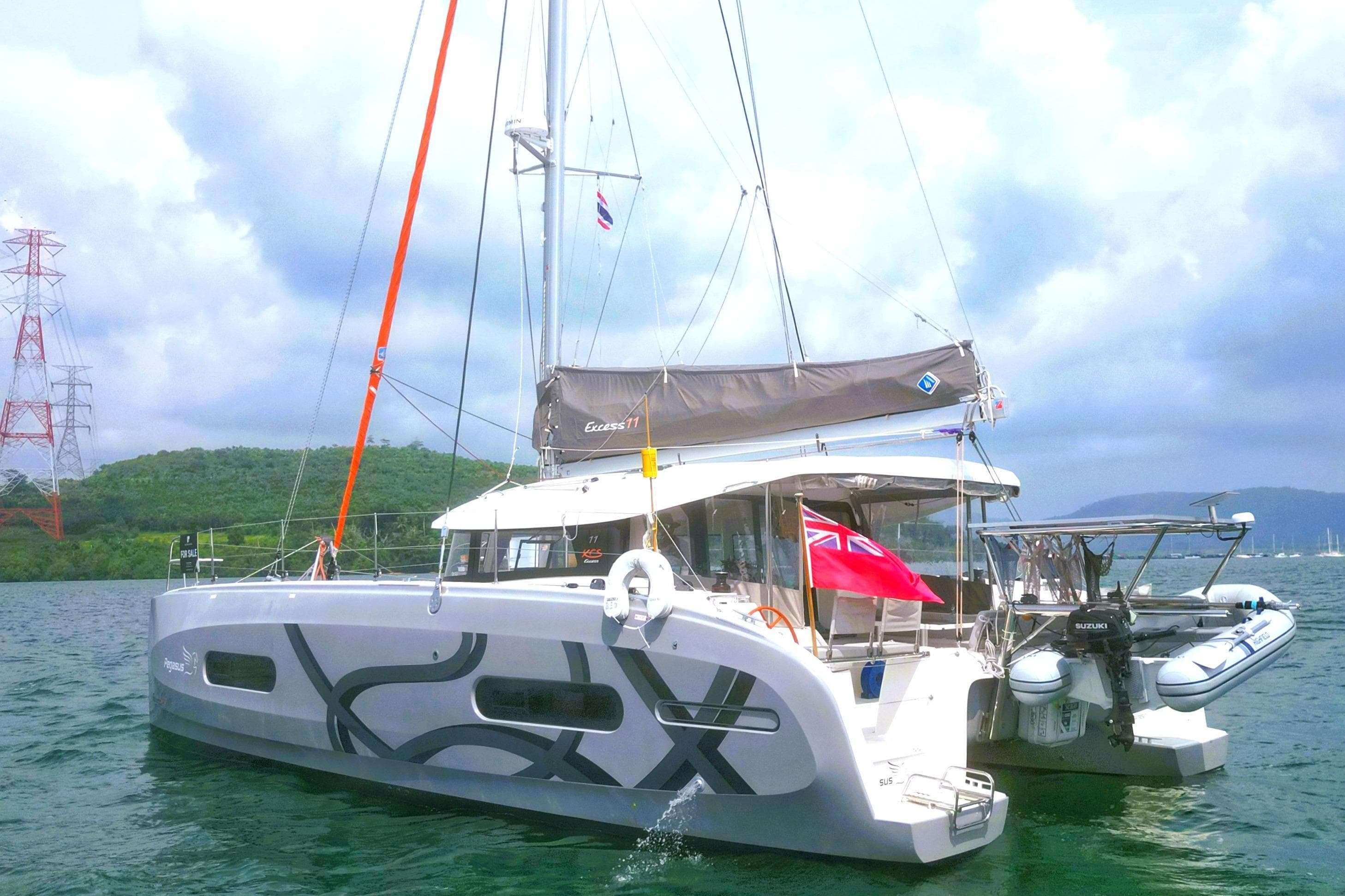 2024 Excess 11 catamaran sailing on a scenic waterway with lush green hills.
