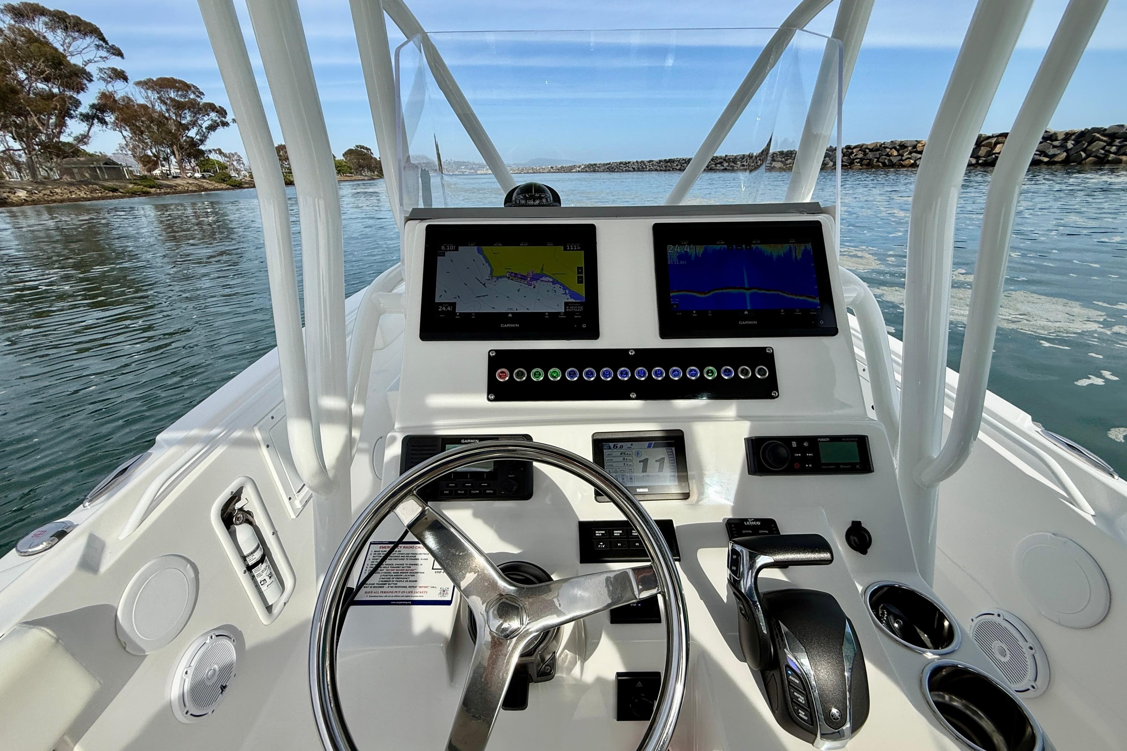 Edgewater 245CC 2023 boat dashboard with navigation screens and steering wheel on calm water.