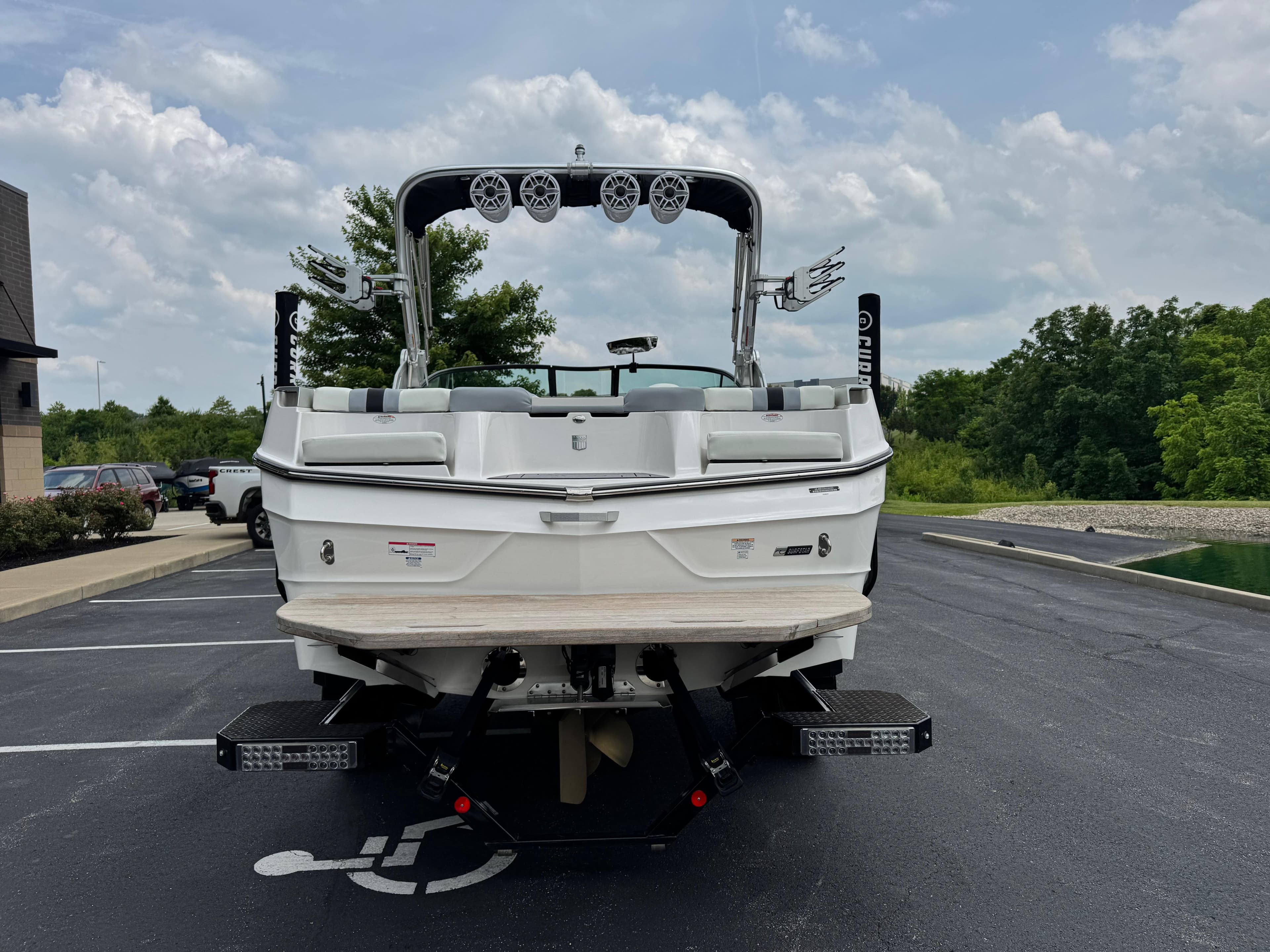 2023 MasterCraft XT23 boat parked on asphalt, rear view with speakers and lush greenery.