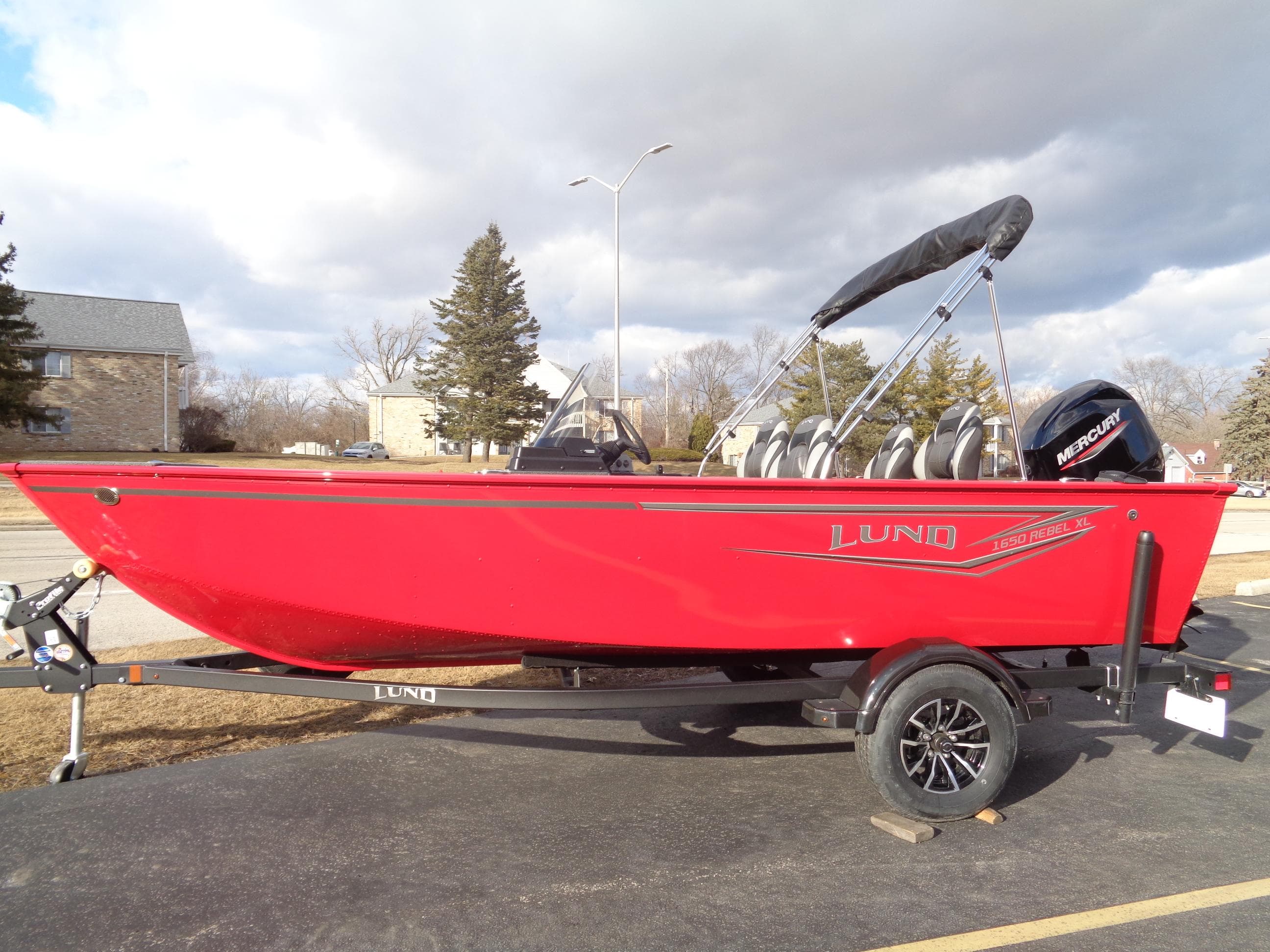 2025 Lund 1650 Rebel XL SS boat in vibrant red on a trailer, parked outdoors.