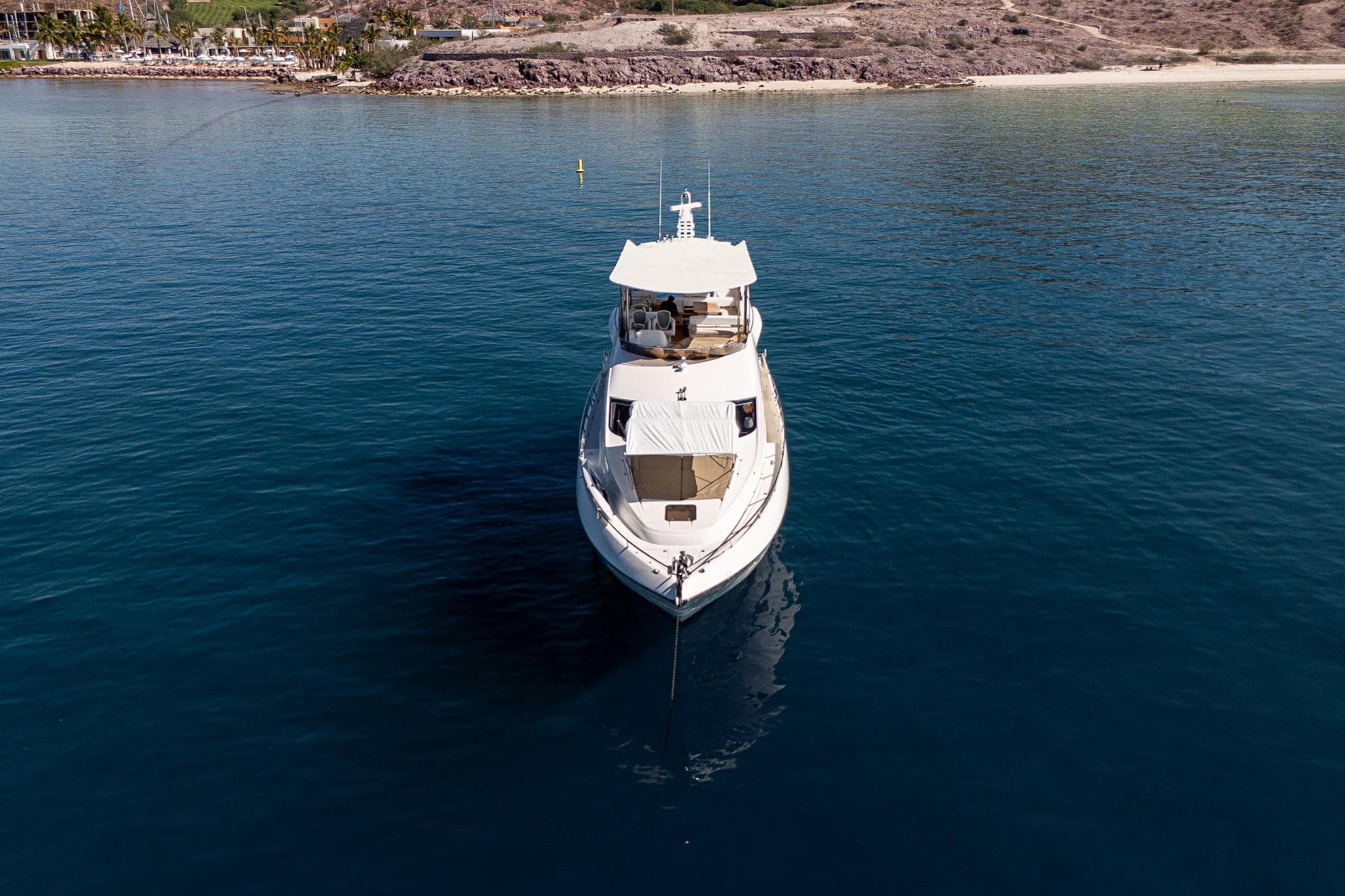 2008 Sunseeker Manhattan 73 yacht anchored in serene blue waters near a rocky coastline.