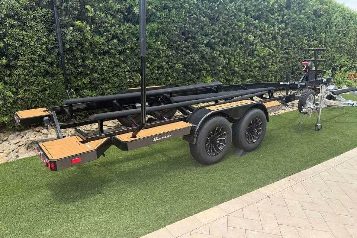 Trailer for 2024 Nautique Super Air Nautique G23 on grass, near hedge.