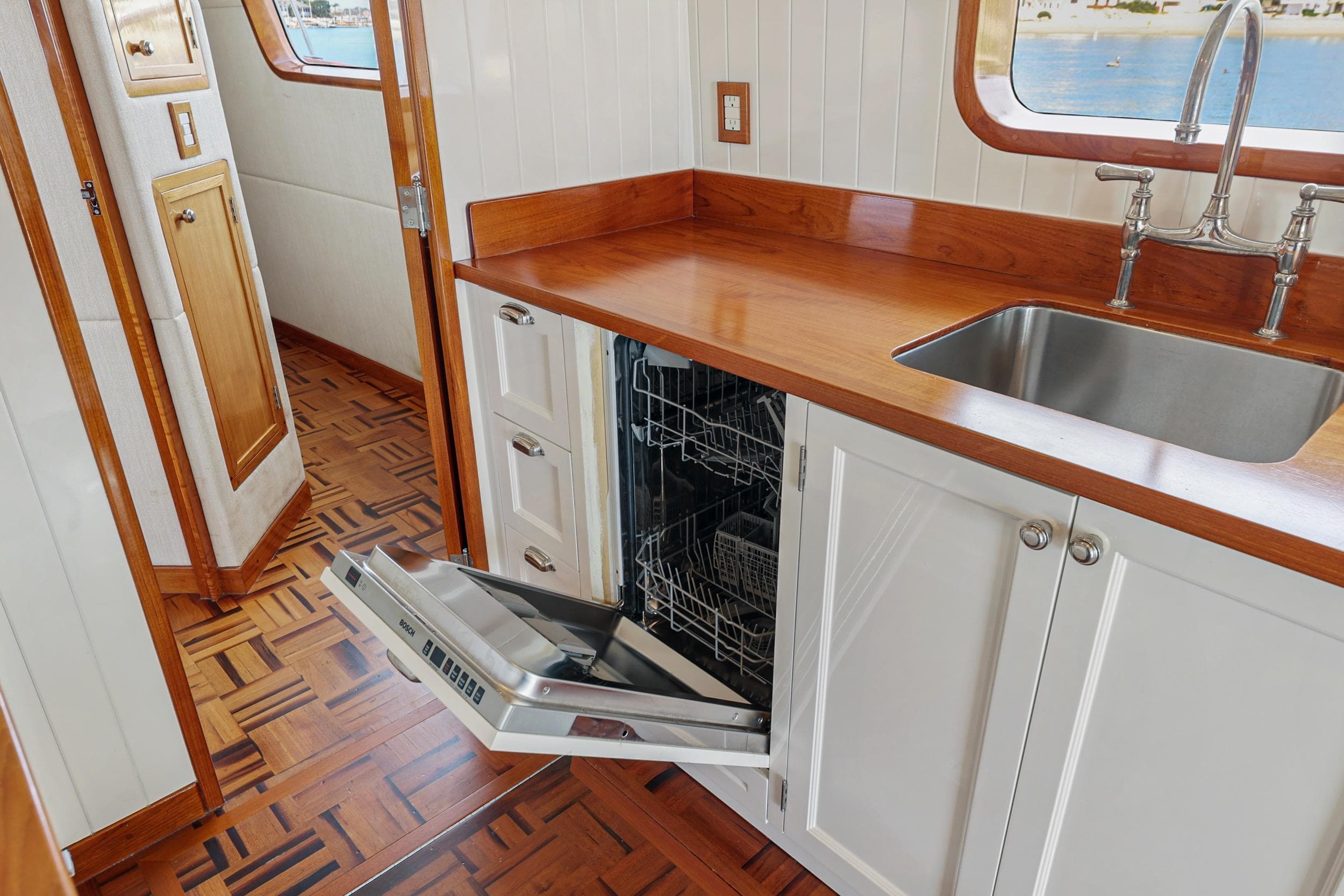 1970 Hargrave Yachtfisher kitchen with open dishwasher, wooden countertops, and stainless steel sink.