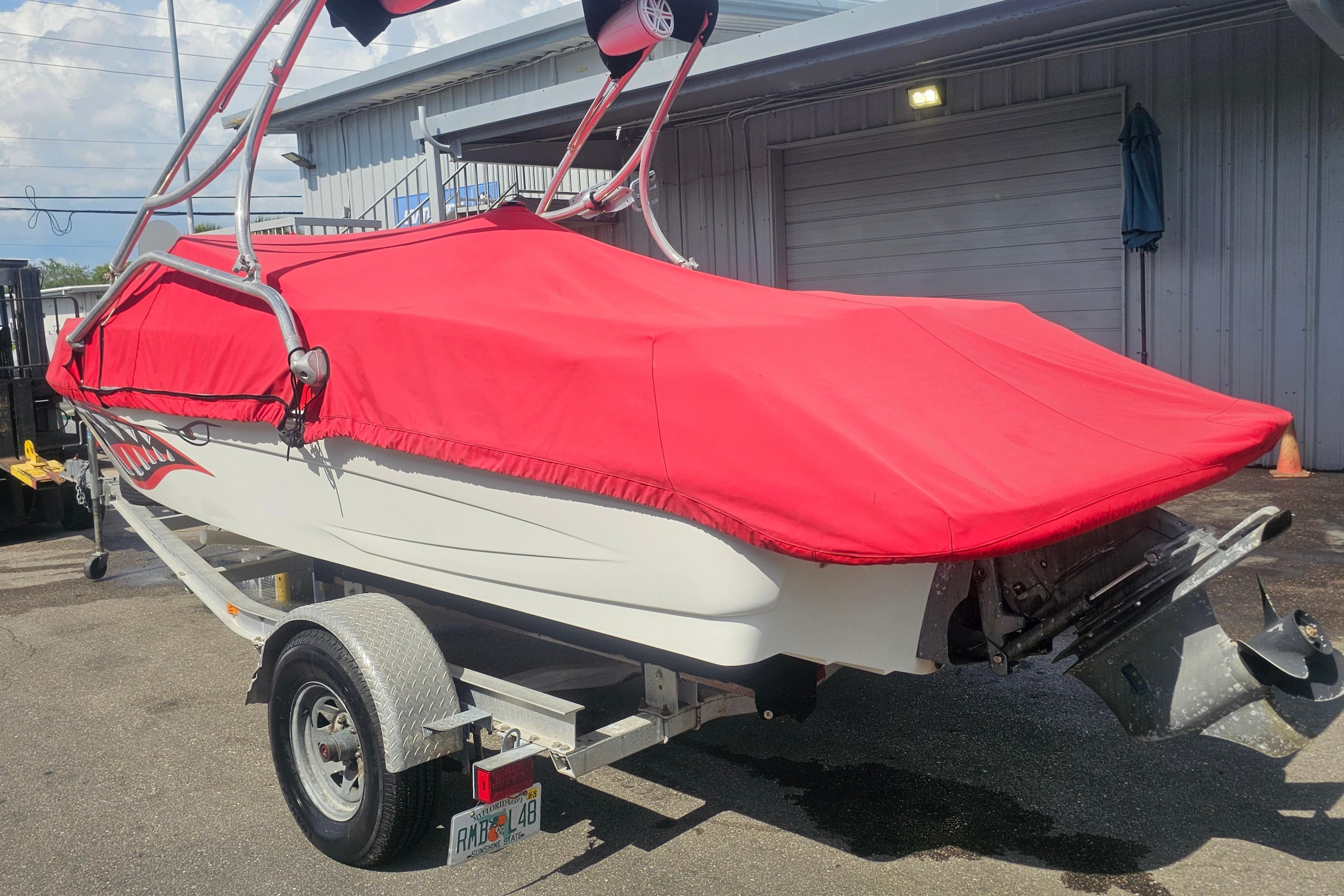 2008 Glastron GT 205 boat with red cover on trailer, parked outside a building.