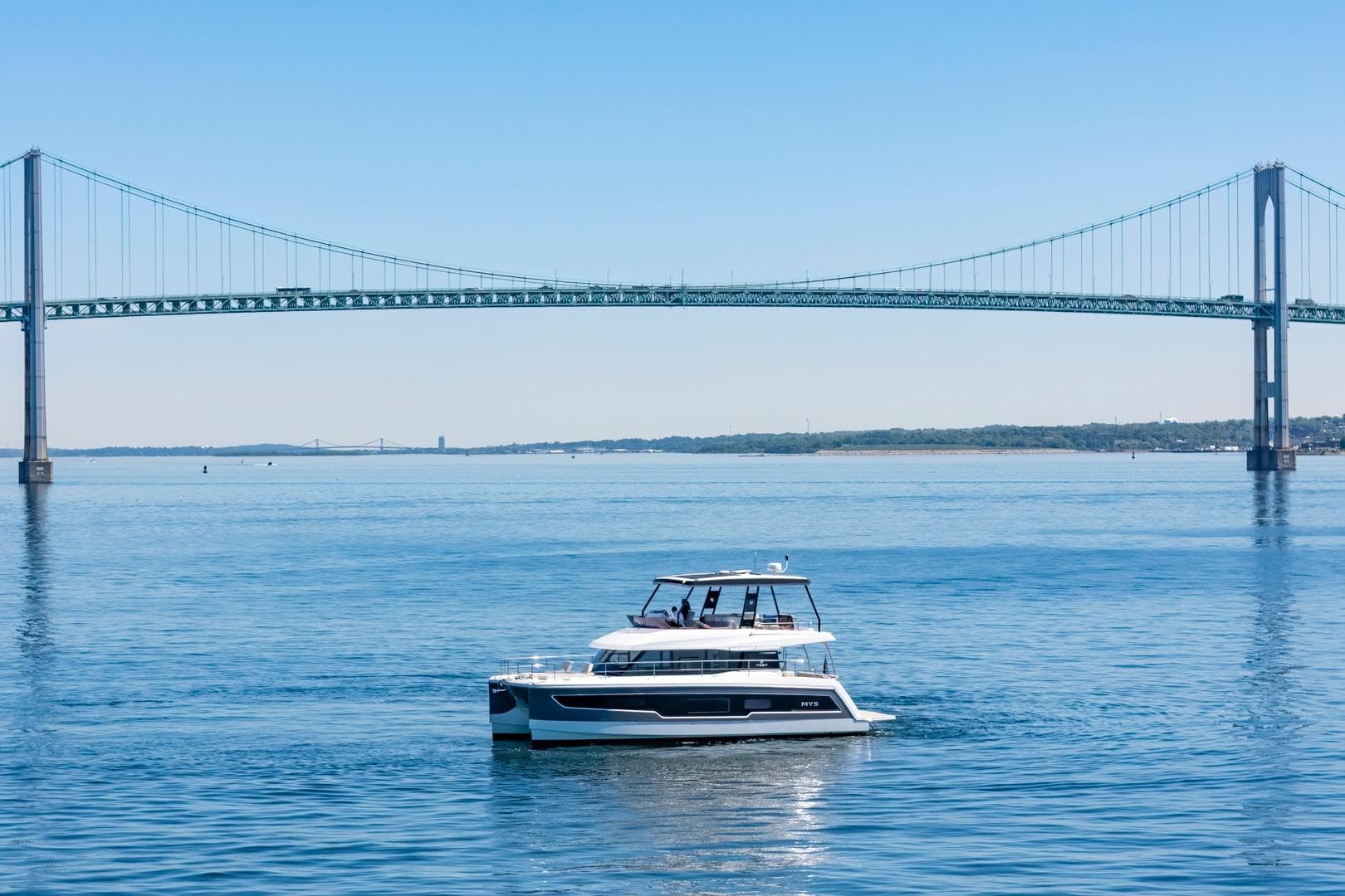 2024 Fountaine Pajot MY5 yacht cruising under a large suspension bridge on a sunny day.