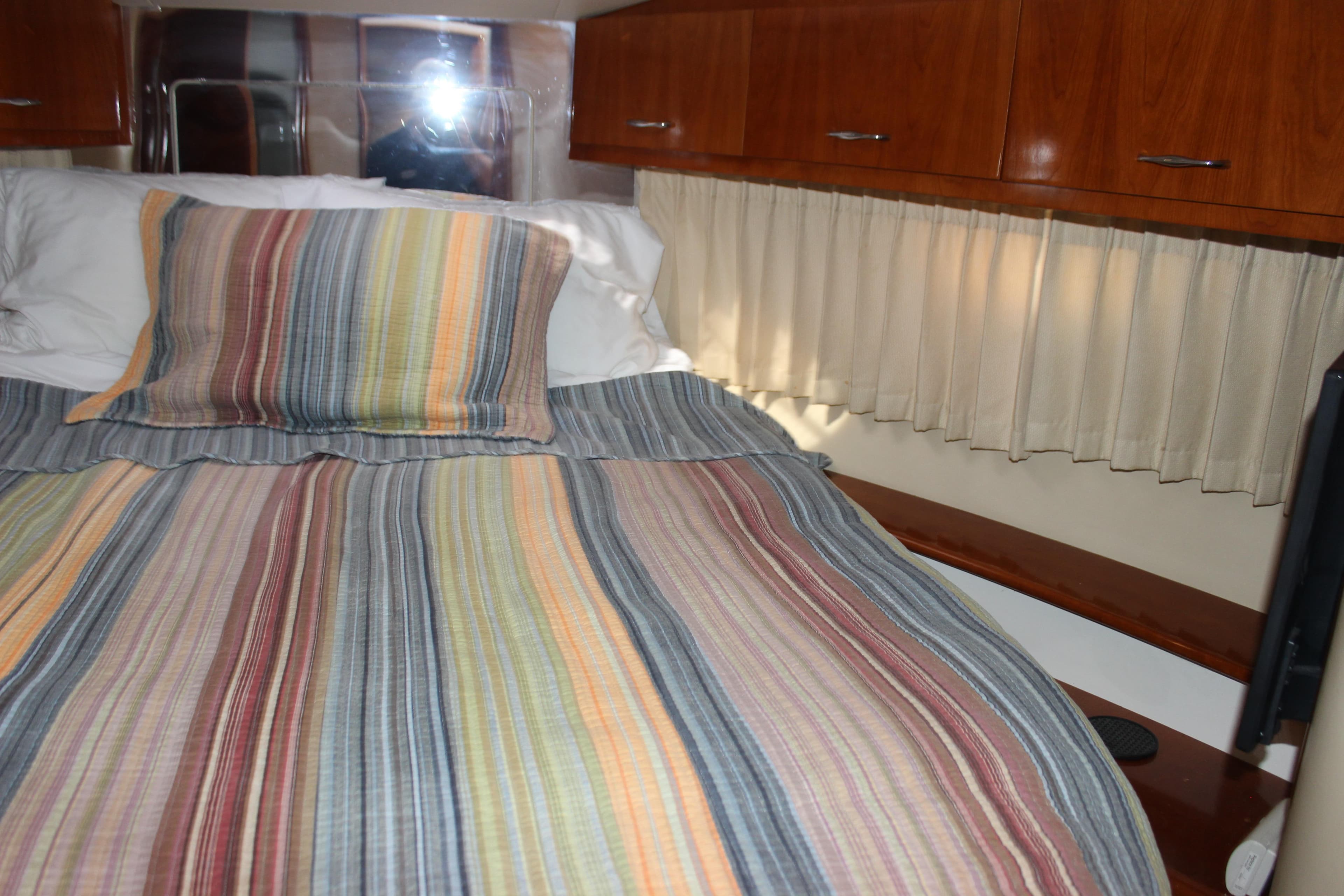 Cozy bedroom in 2003 Carver 36 Super Sport with striped bedding and wooden cabinets.