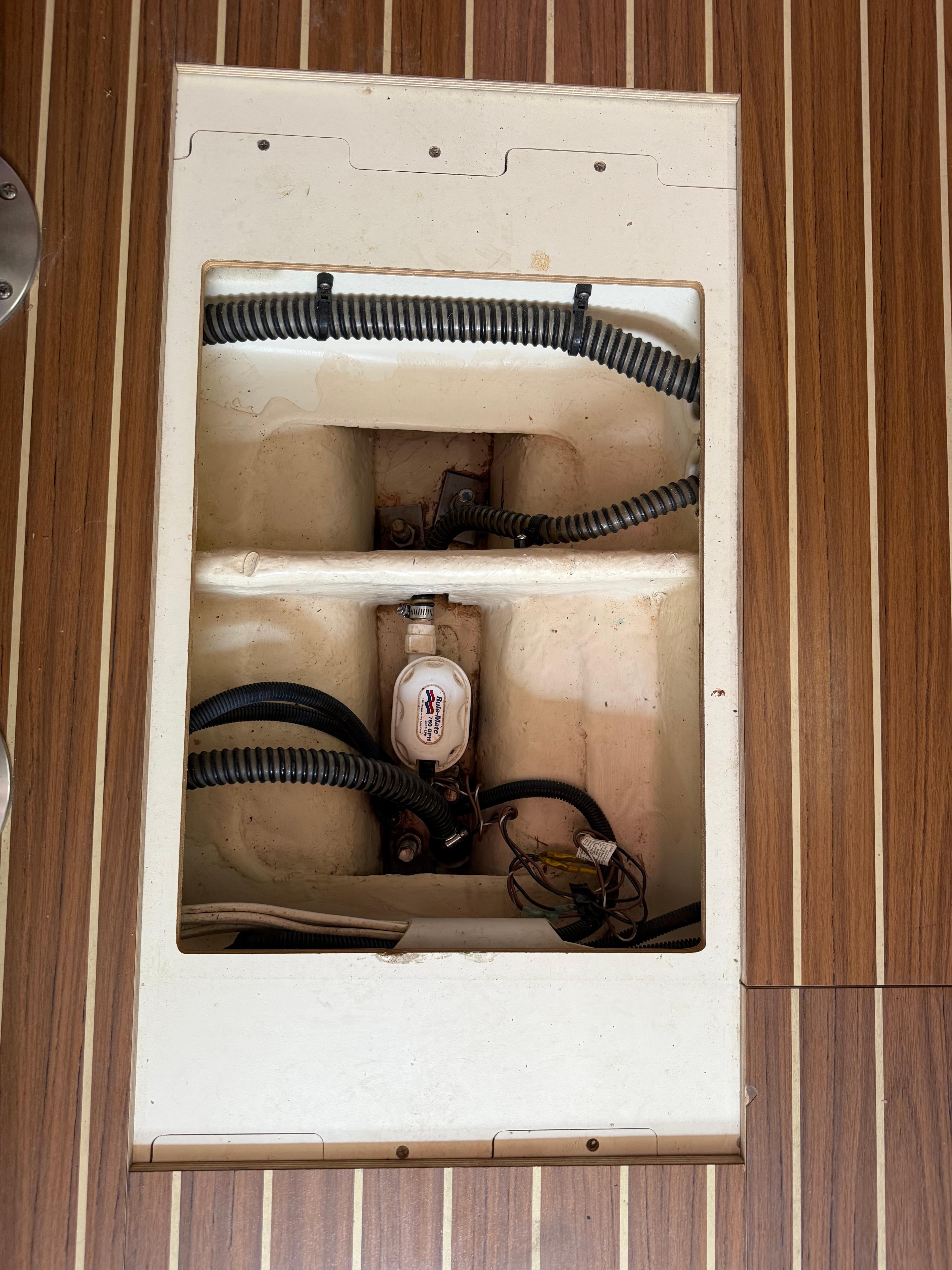 Bilge compartment of a 2005 Hunter 33 sailboat with visible hoses and pump.