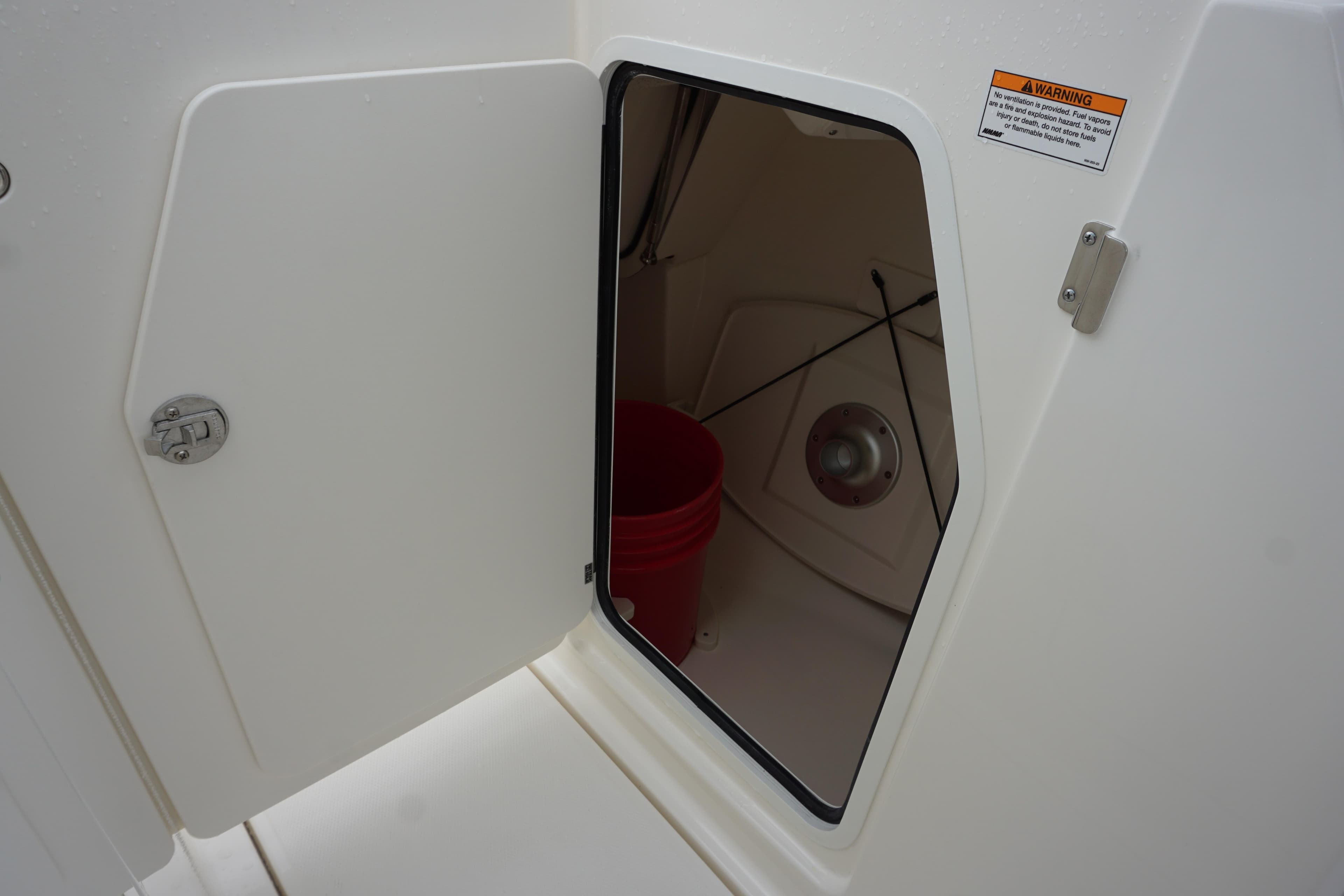 Open storage compartment on 2026 Boston Whaler 240 Vantage boat, featuring a red bucket inside.