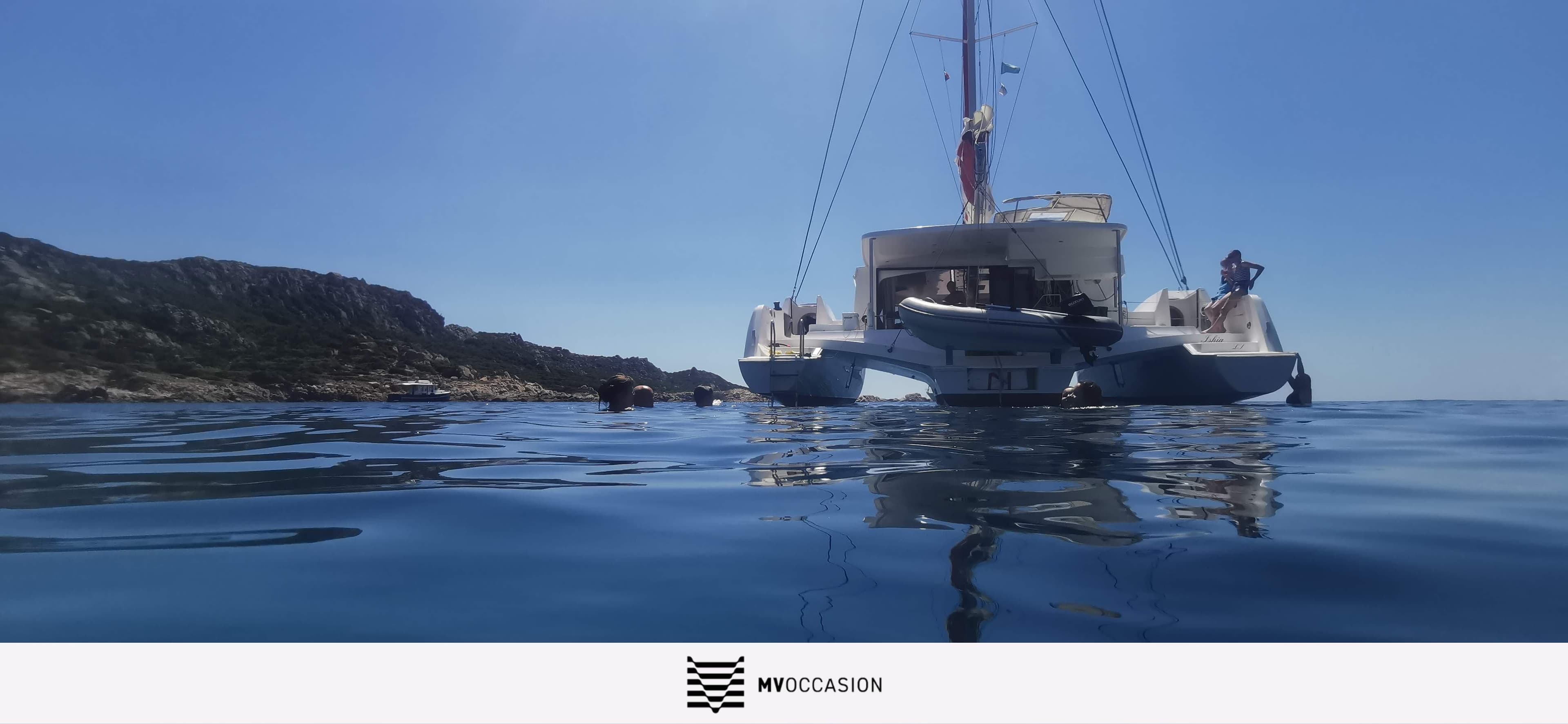 Trimaran sailing near rocky coastline under clear blue sky, NEEL 47 model, 2021.