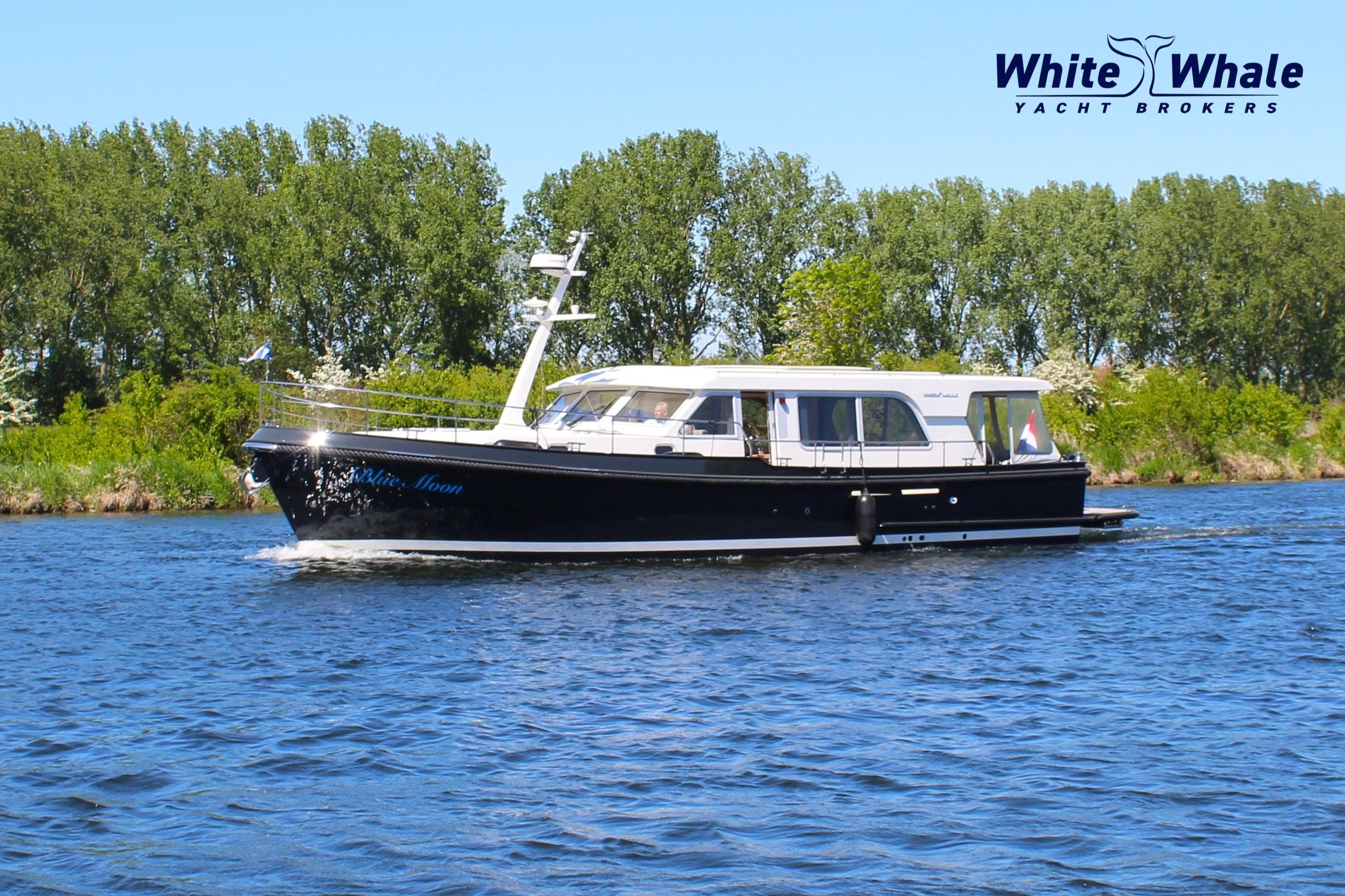 2023 Linssen Grand Sturdy 500 Sedan cruising on a river, surrounded by lush greenery.