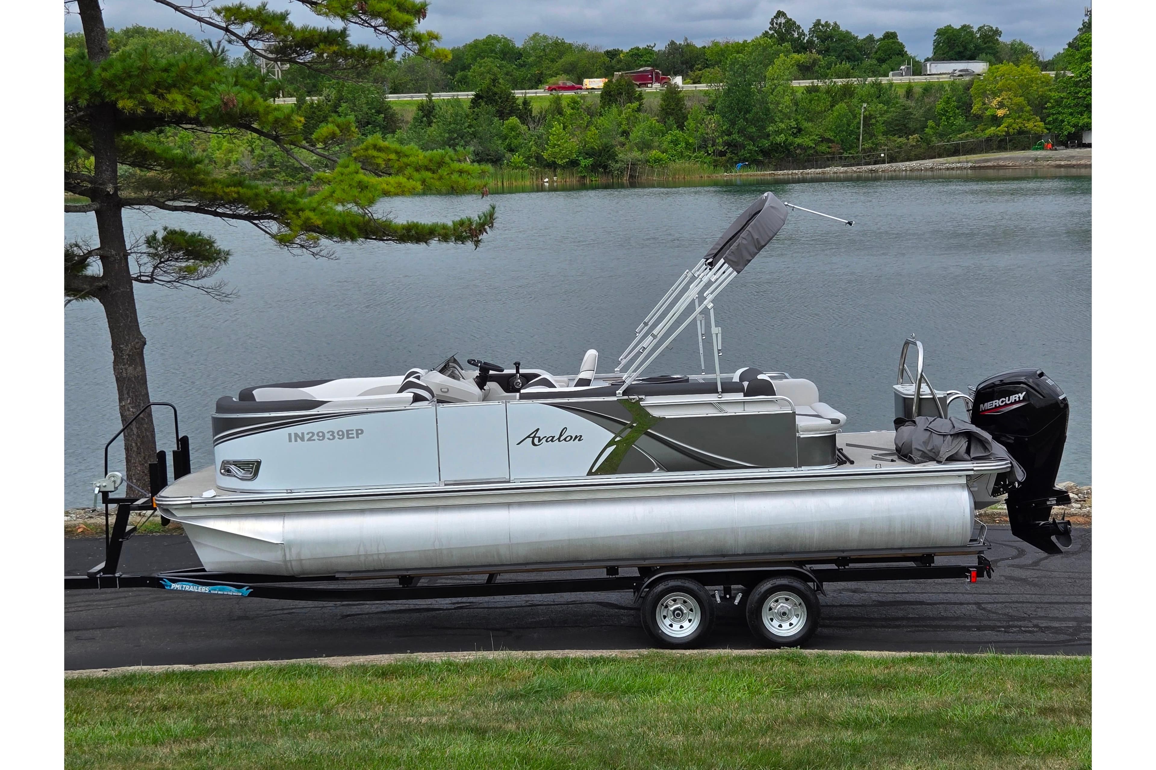2024 Avalon LSZ Cruise Bench pontoon boat on trailer by a scenic lake.