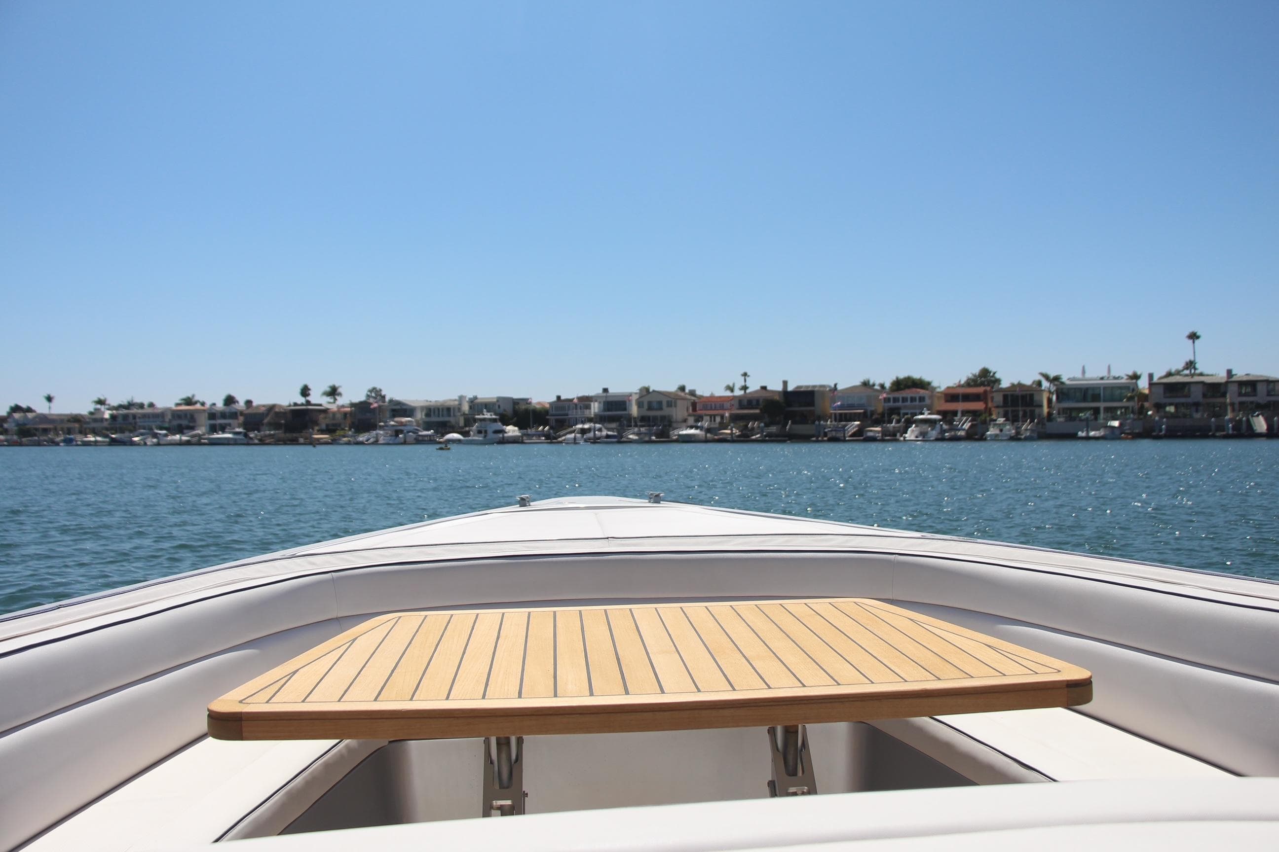 Bow view of 2017 Maori 50 boat with wooden table, coastal houses in background.