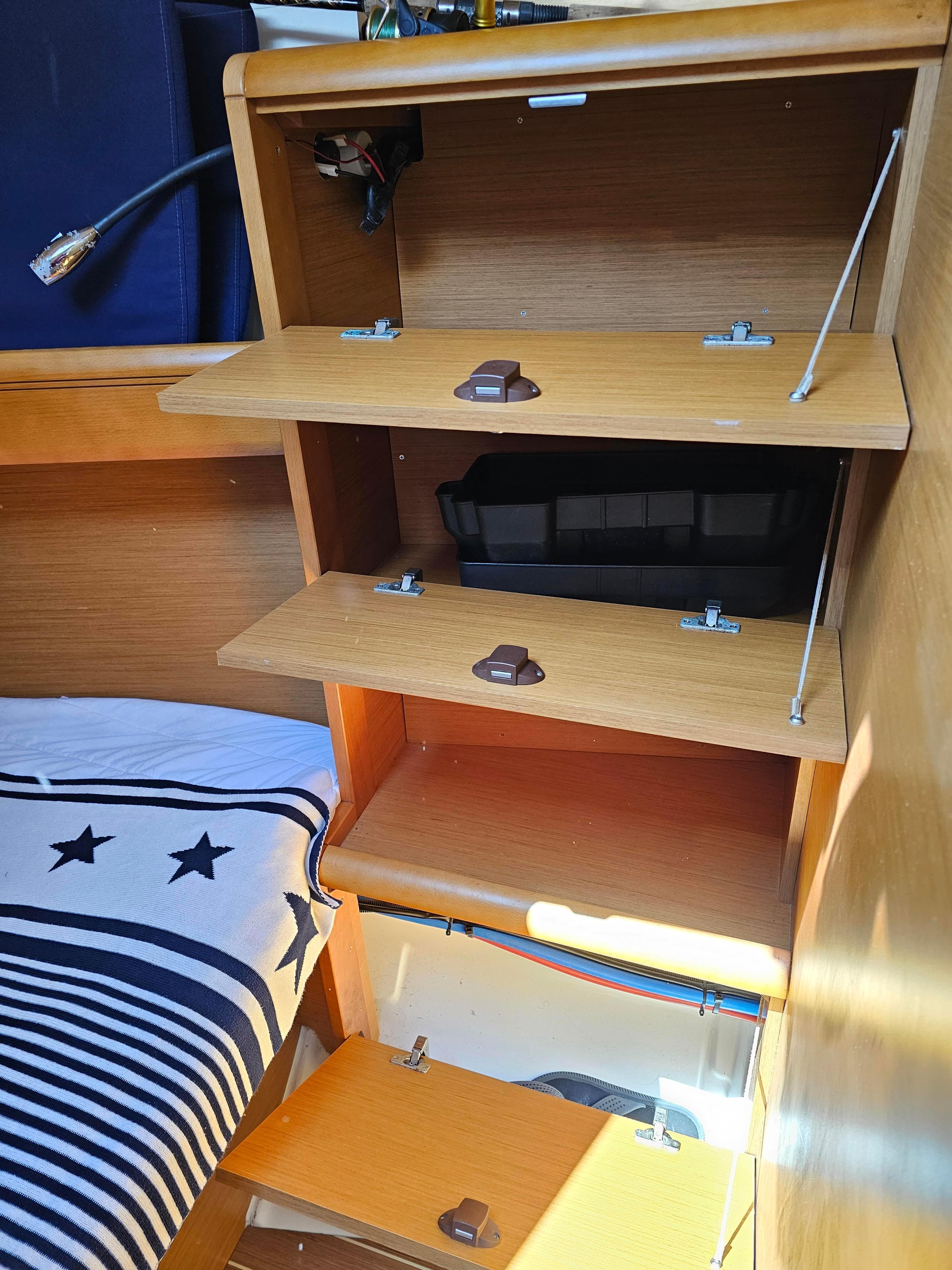 Interior storage shelves on a 2016 Jeanneau 379 sailboat, featuring wooden compartments and nautical bedding.