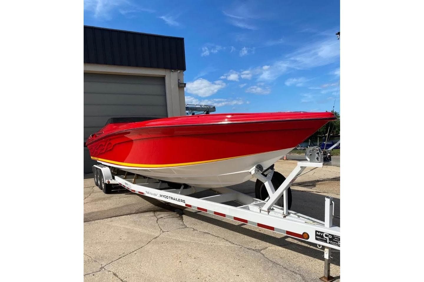 Red 2005 Hustler 388 SLINGSHOT boat on trailer, parked outdoors under blue sky.