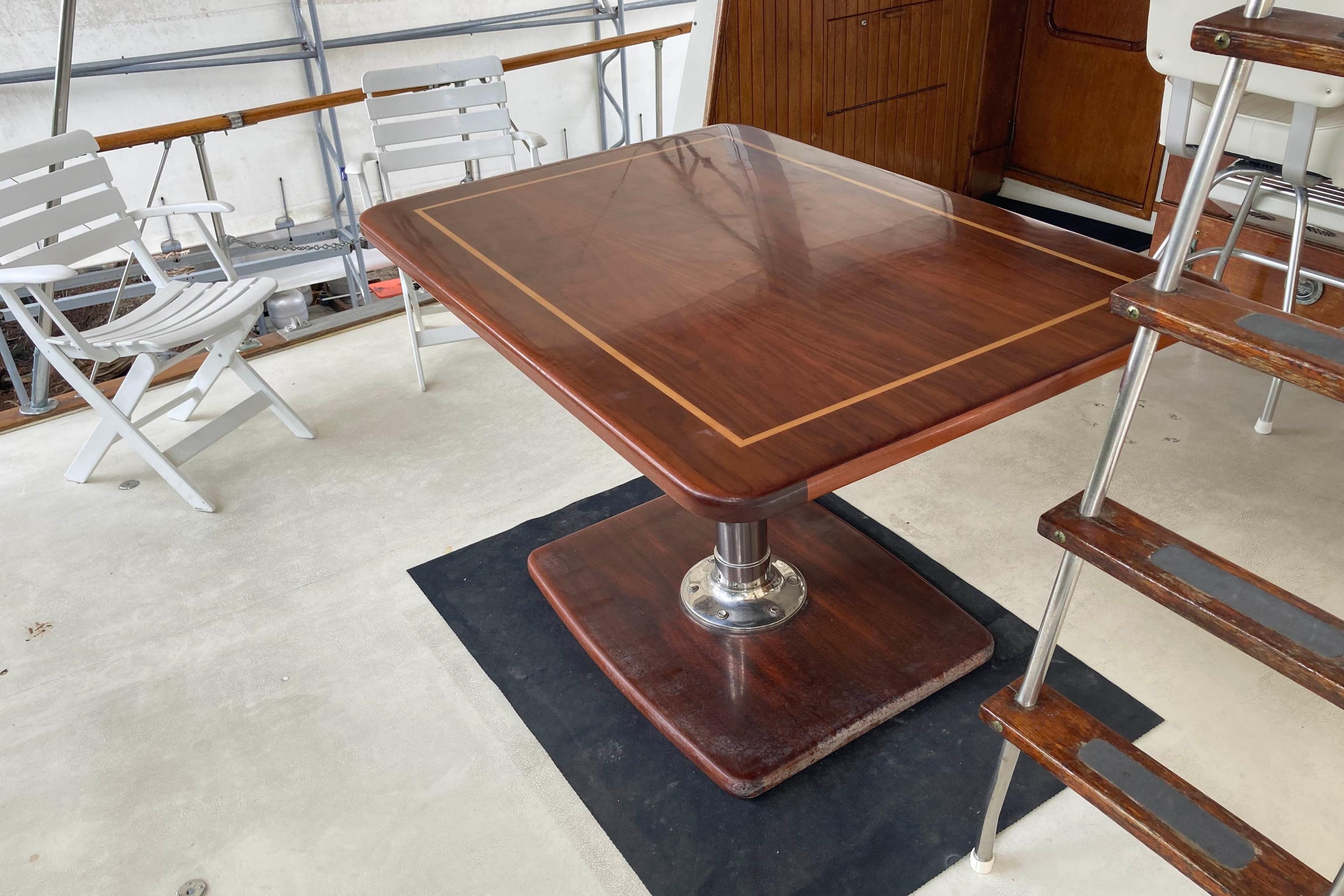 Elegant wooden table on 1972 Chris-Craft 45 Commander yacht deck, surrounded by chairs and stairs.