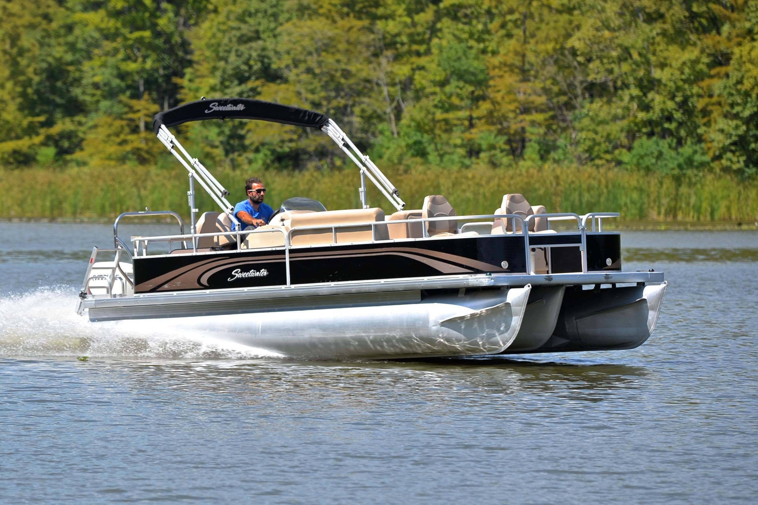 2014 Godfrey SWEETWATER 2486 pontoon boat cruising on a lake with lush greenery.