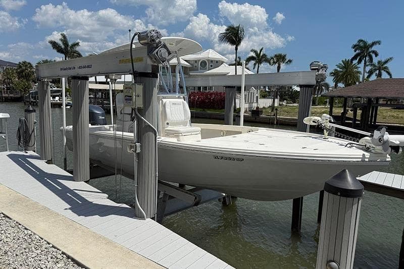 2020 Pathfinder 2500 Hybrid boat on lift, docked by waterfront homes and palm trees.