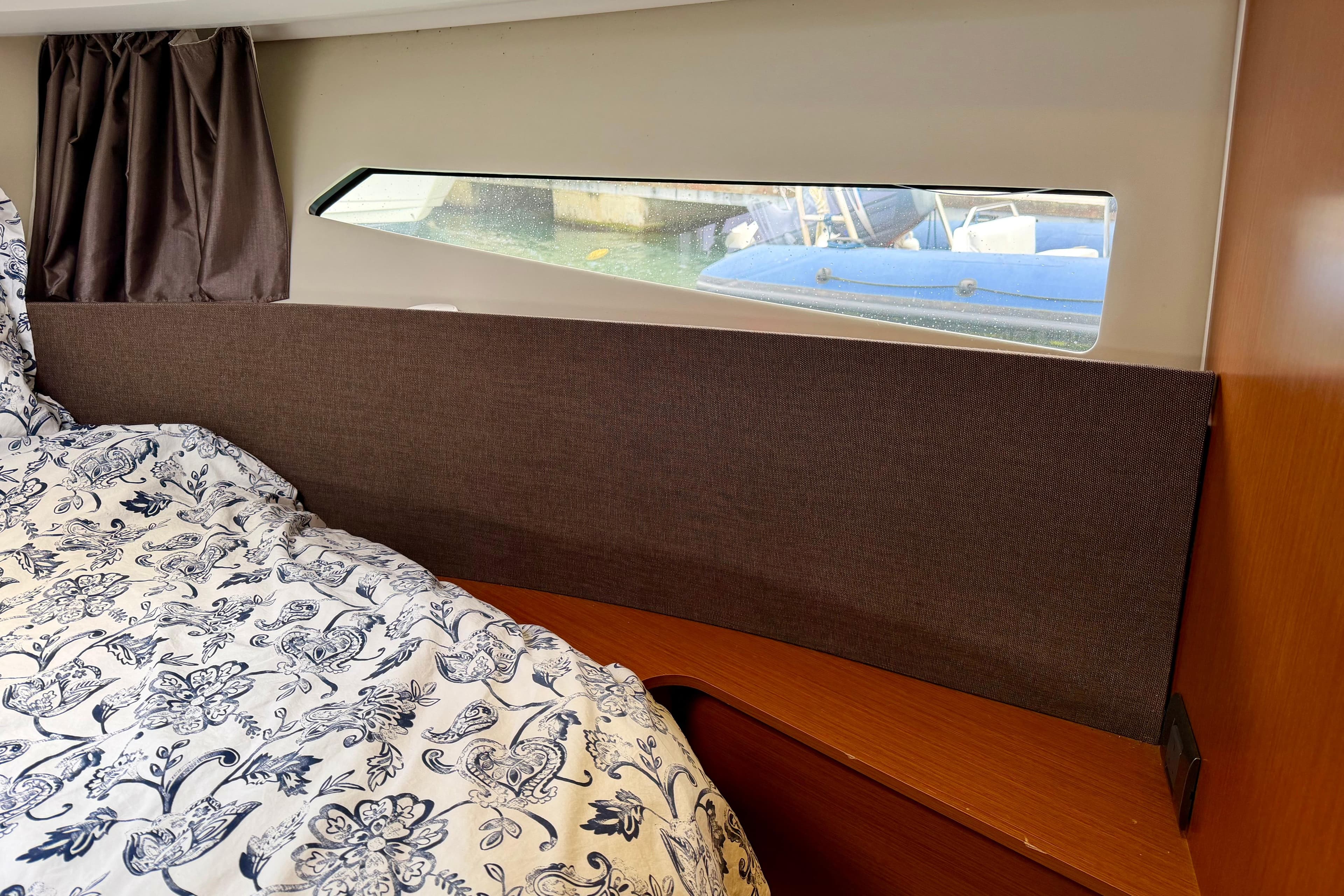 Cozy cabin interior of 2013 Jeanneau NC 9 with floral bedding and window view.