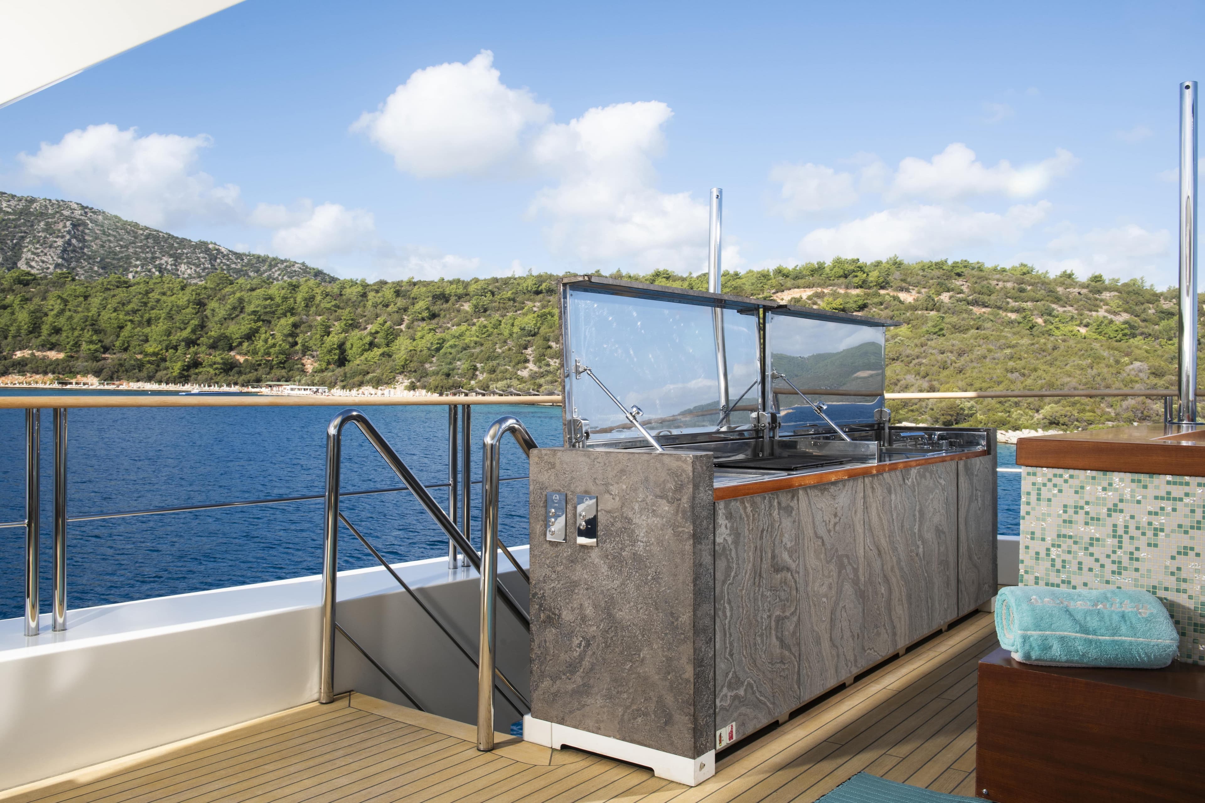 Luxurious Mondomarine SF40 yacht deck with outdoor kitchen, overlooking serene blue waters and lush landscape.