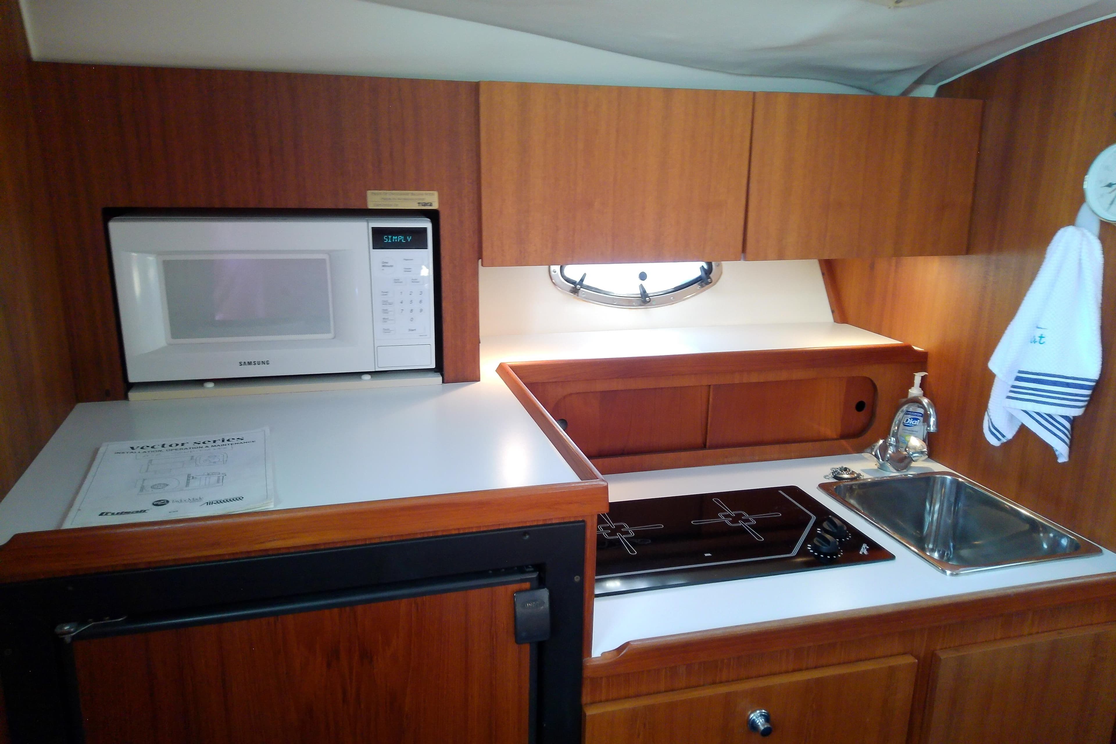 Compact kitchen in a 2000 Tiara Yachts 3100 Open, featuring microwave, stove, and sink.