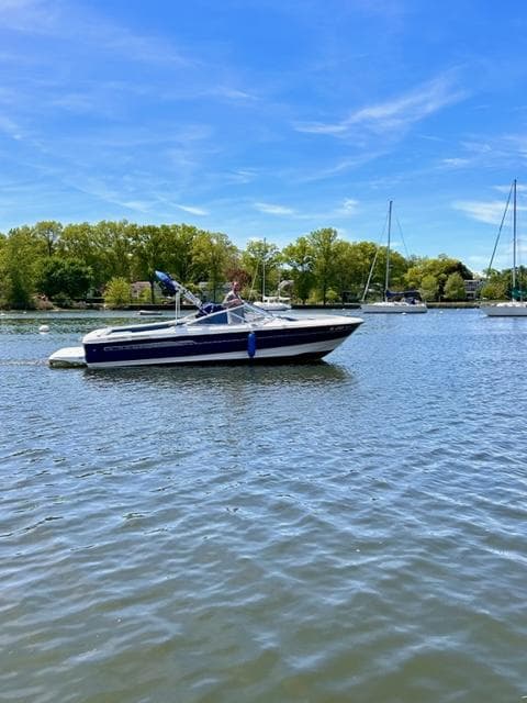 2006 Bayliner 215 Classic boat on a calm lake with trees in the background.