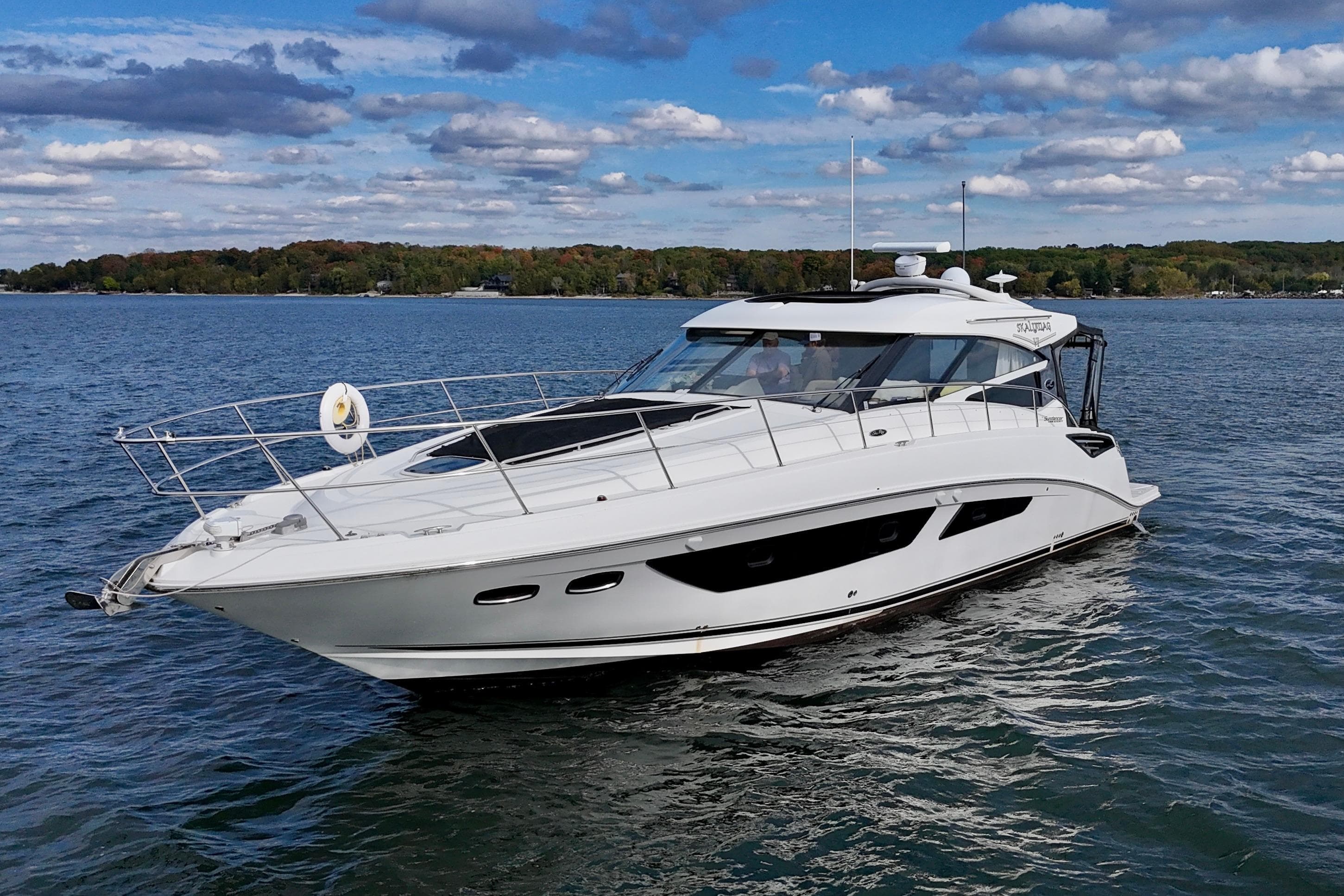 2015 Sea Ray 470 Sundancer yacht cruising on a serene lake under a partly cloudy sky.