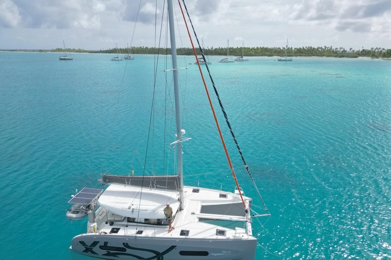 2024 Excess 11 catamaran sailing in turquoise waters with distant islands.