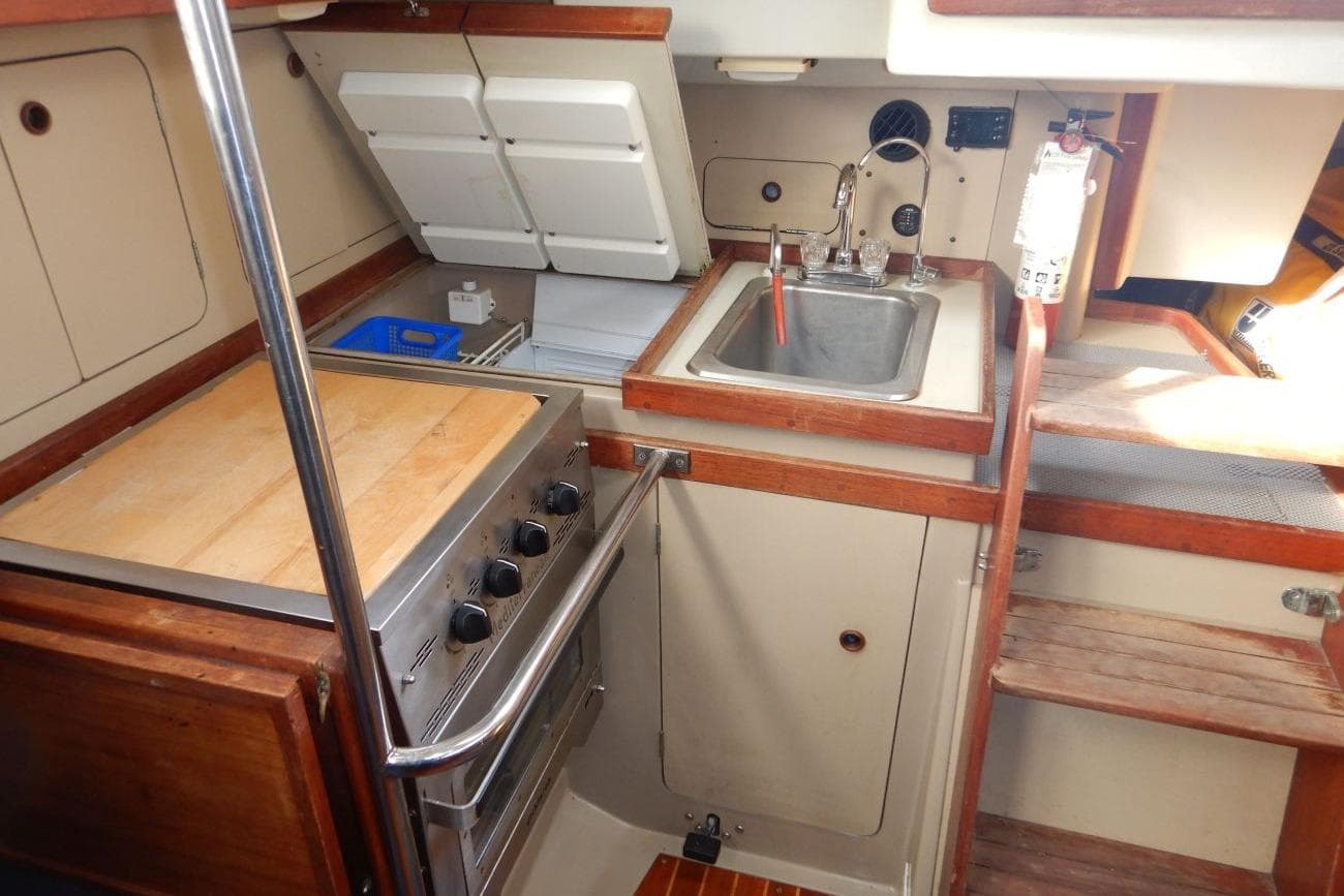 1985 C&C 332 Sloop galley with stove, sink, and wooden cabinetry.