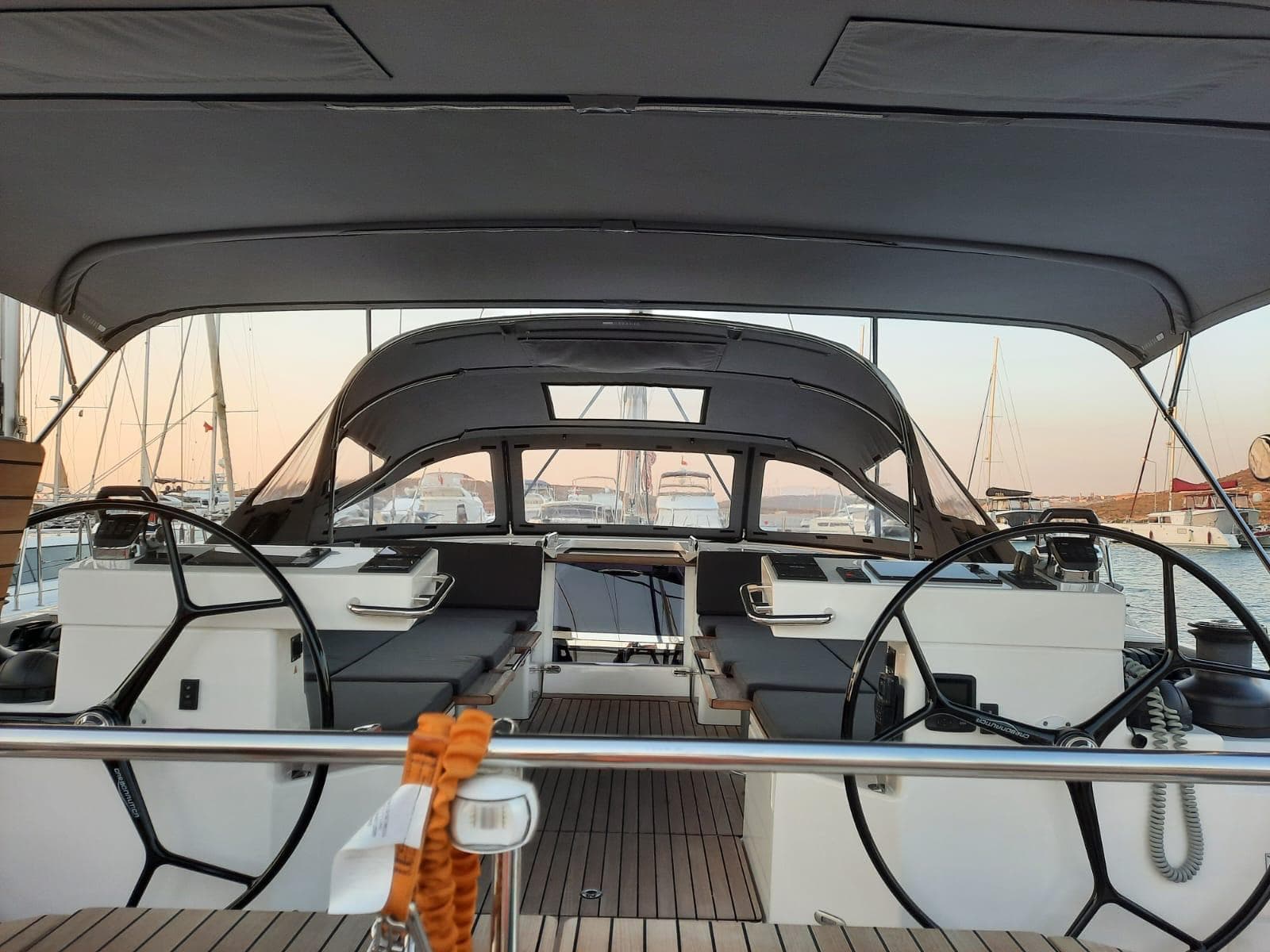 Modern Bavaria C57 yacht cockpit with dual steering wheels, docked at sunset, 2023 model.