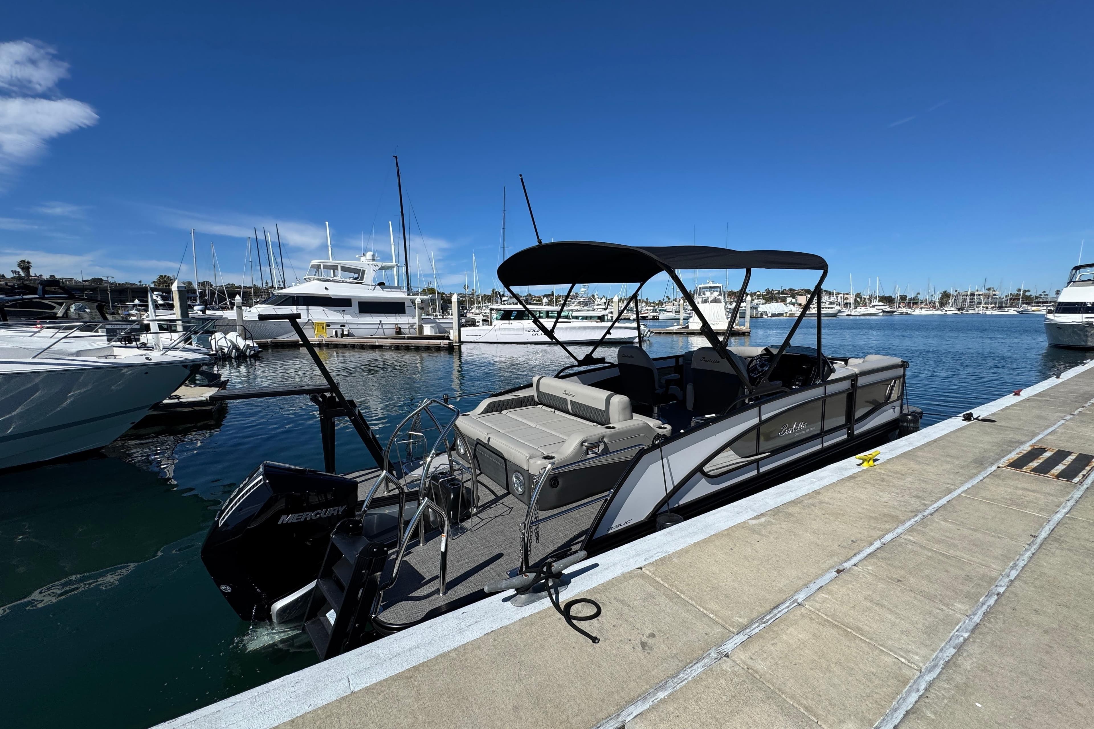 2026 Barletta Lusso 23UC pontoon boat docked at a marina under clear blue skies.