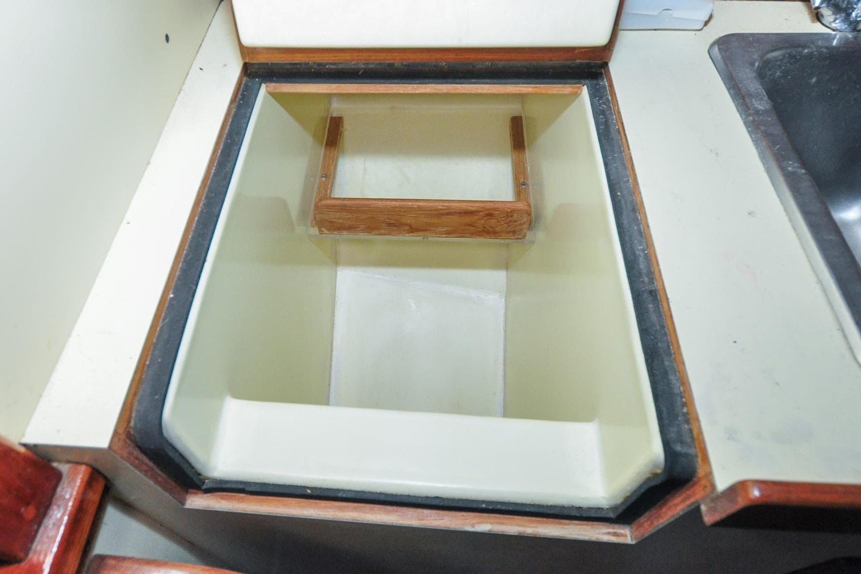 Icebox interior on 1987 Nauset Coastal 27 boat, featuring wooden handle and white lining.