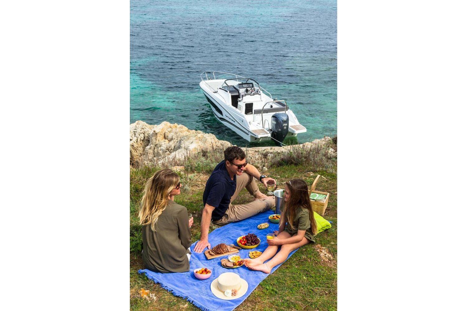Family enjoying a picnic by the sea with a 2024 Jeanneau Cap Camarat 7.5 WA boat.