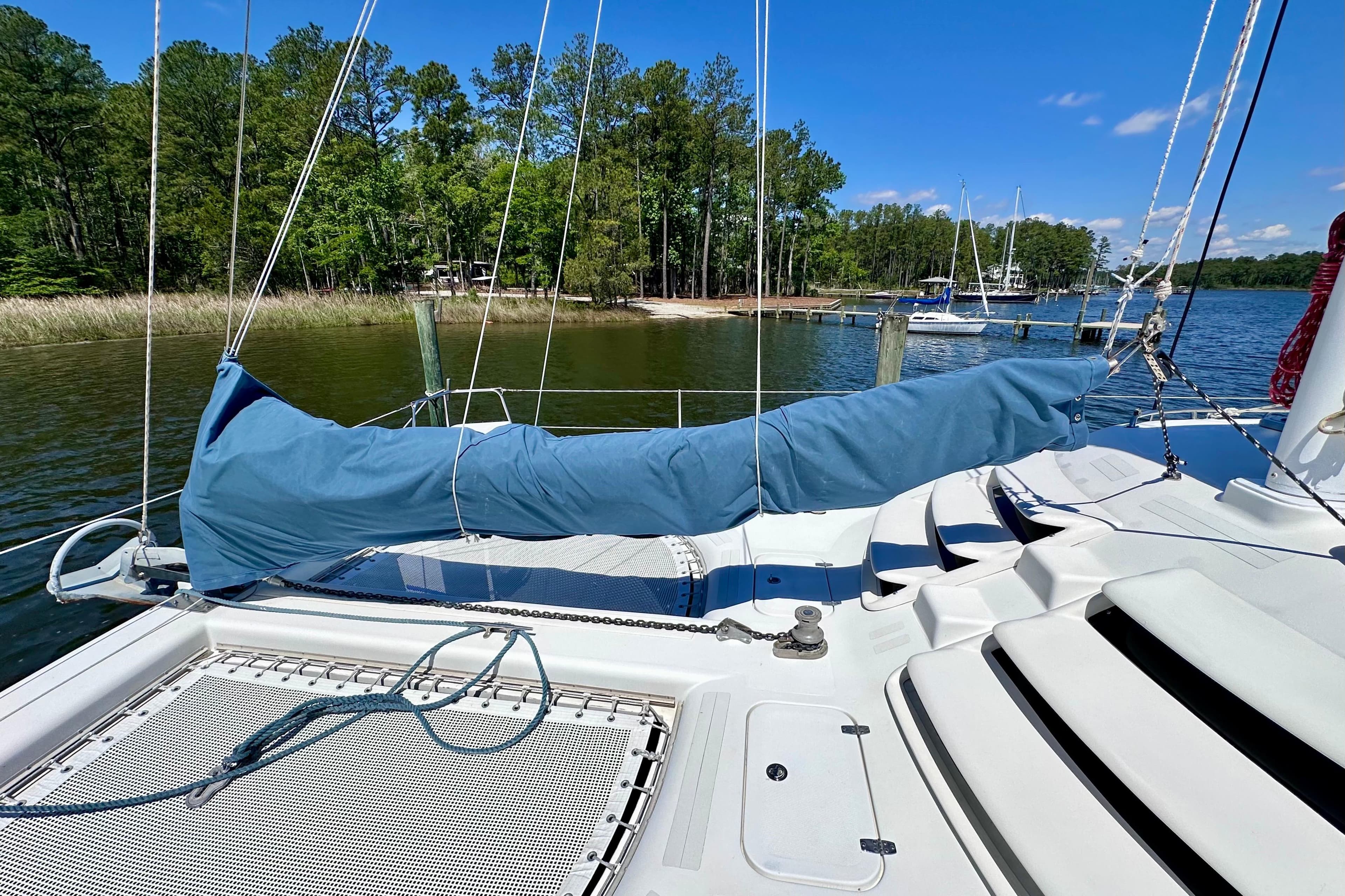 Sailboat deck of 1998 Manta 40, docked by a serene lakeside with lush greenery.