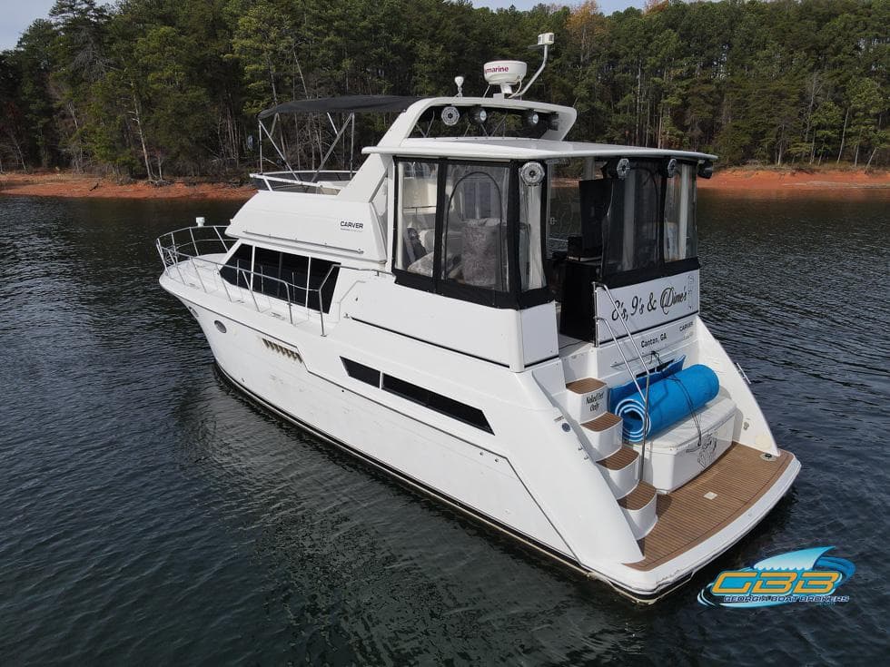 1998 Carver 405 Aft Cabin yacht on a serene lake with forested shoreline.