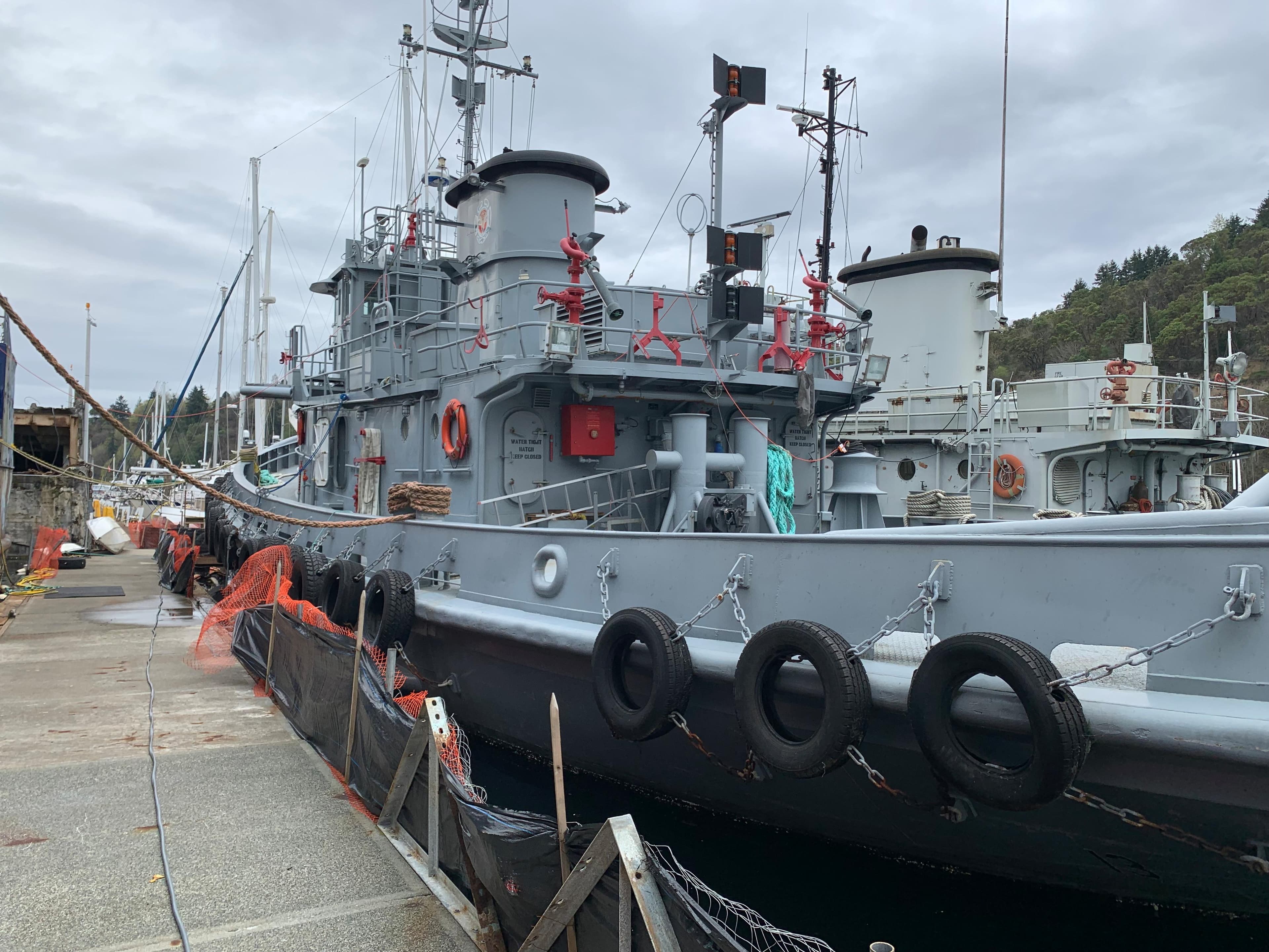1955 L-T 100 Steel Army Tugboat docked at a harbor, overcast sky.