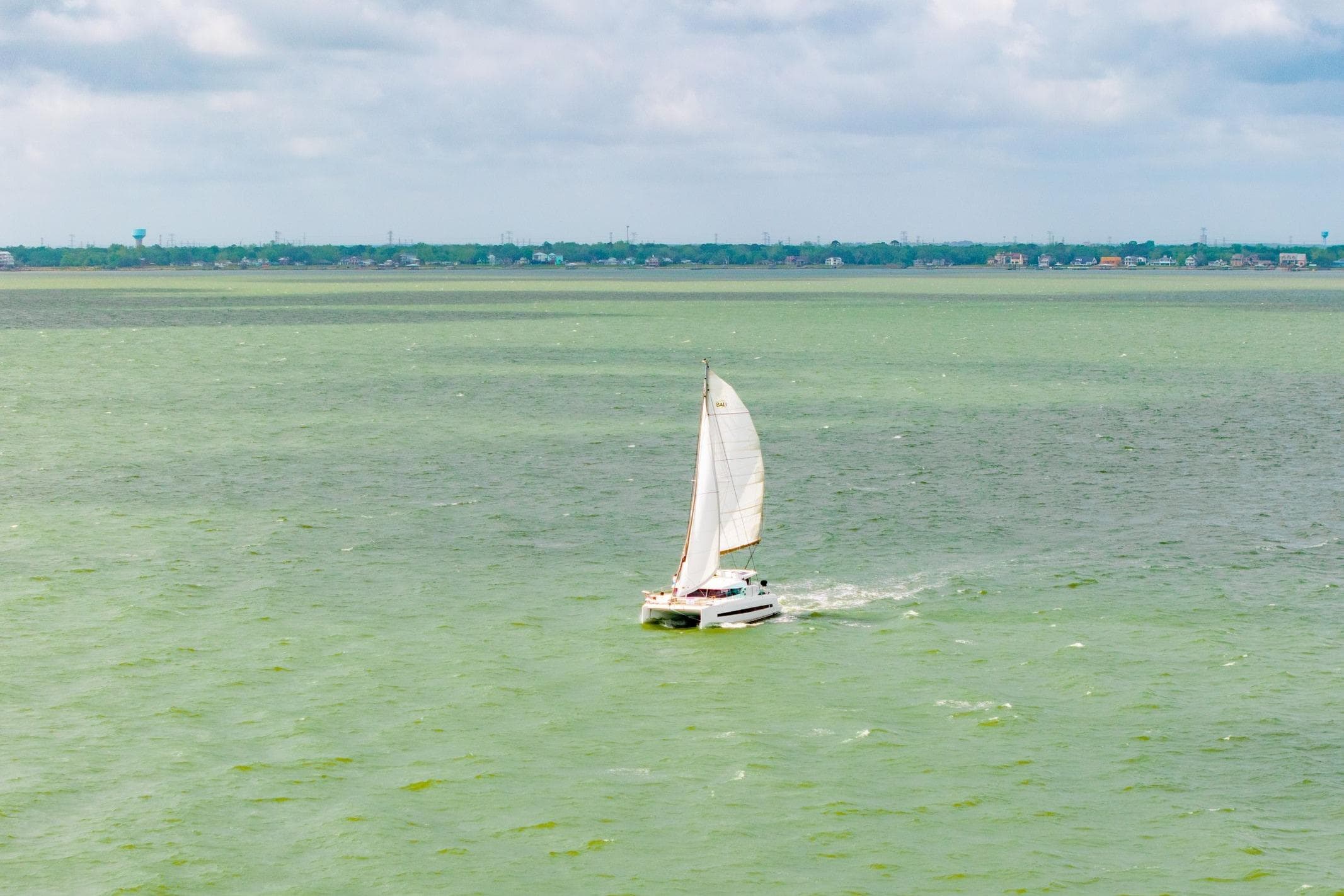 Sailboat Bali 4.1 cruising on calm green waters under cloudy skies, 2019 model.