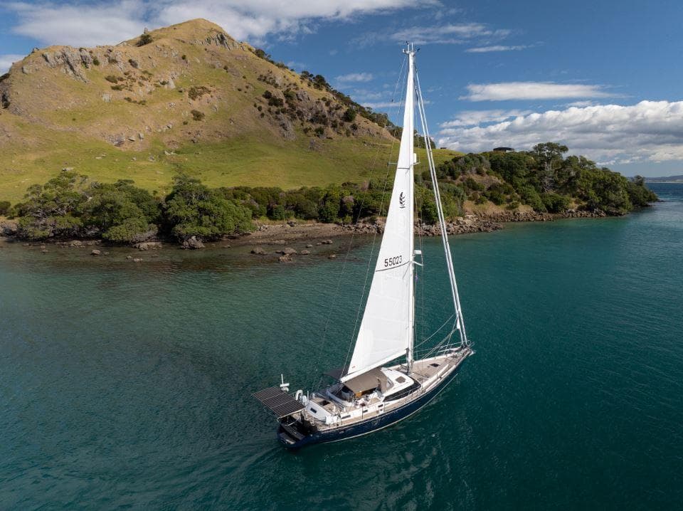 Sailing yacht Discovery 55 (2008) cruising near a lush, hilly island.