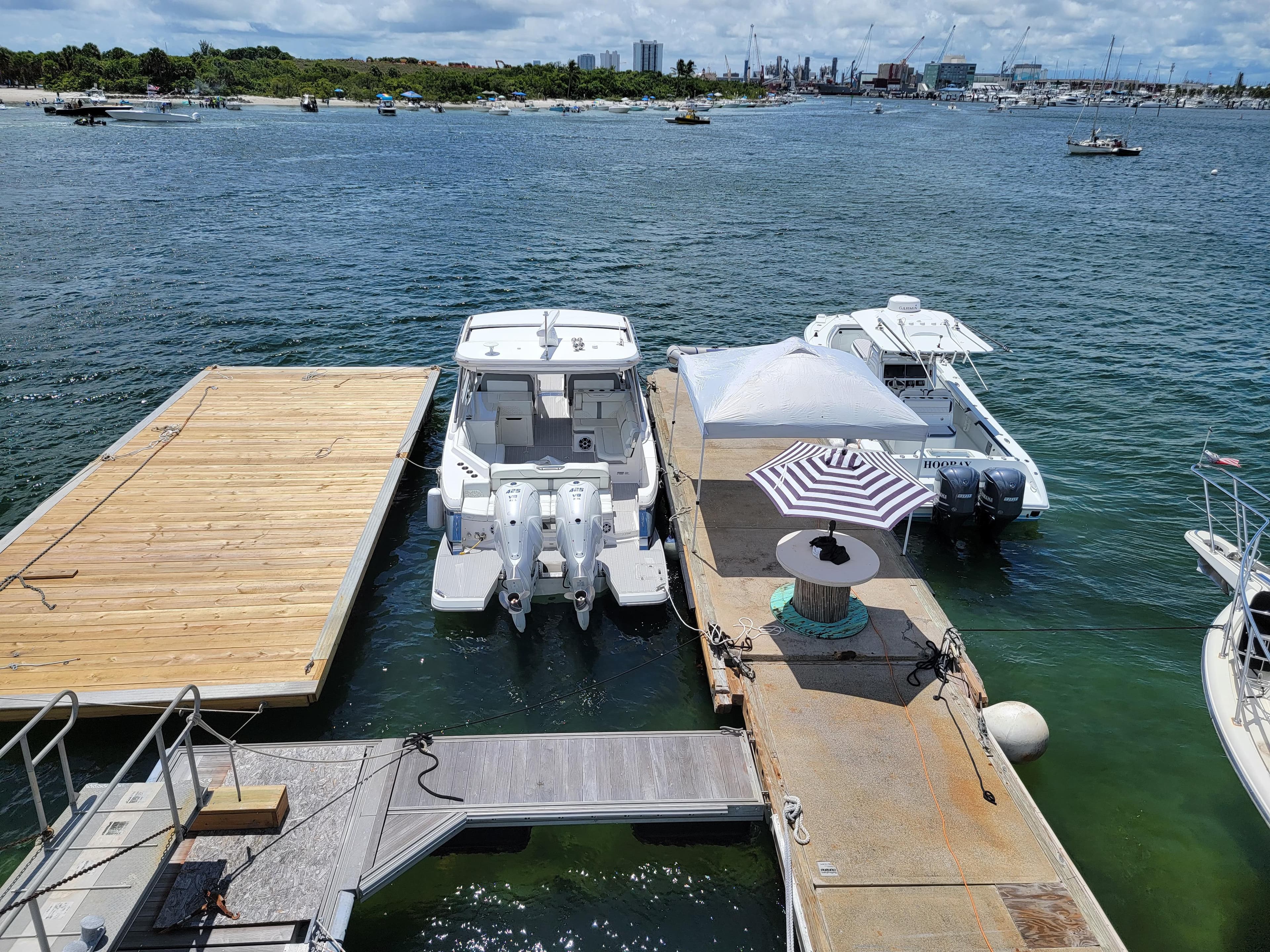 Floating home docked with boats, featuring a striped umbrella, on a sunny waterfront.