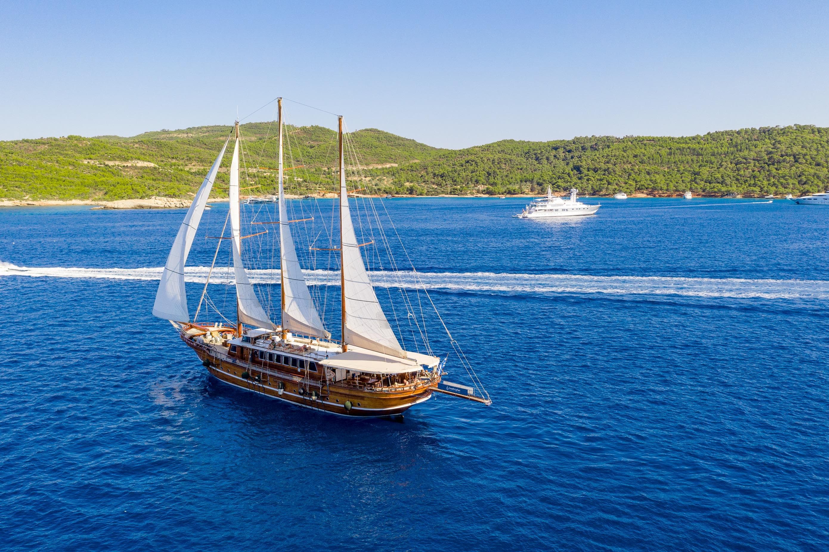 Sailing Gulet Custom 2002 on blue sea with lush green coastline in background.