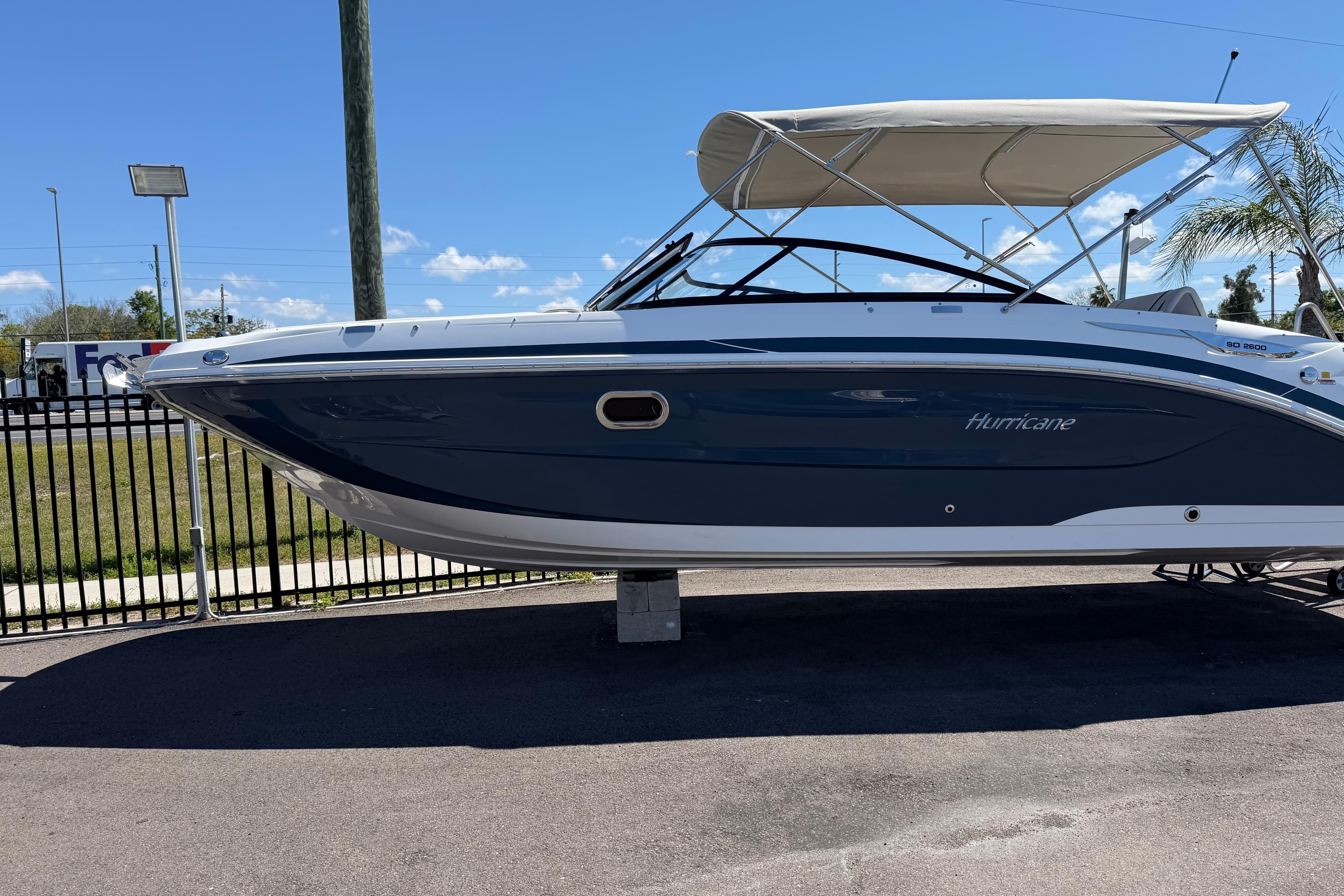 2026 Hurricane SunDeck 2600 OB boat with canopy, parked on pavement under clear blue sky.