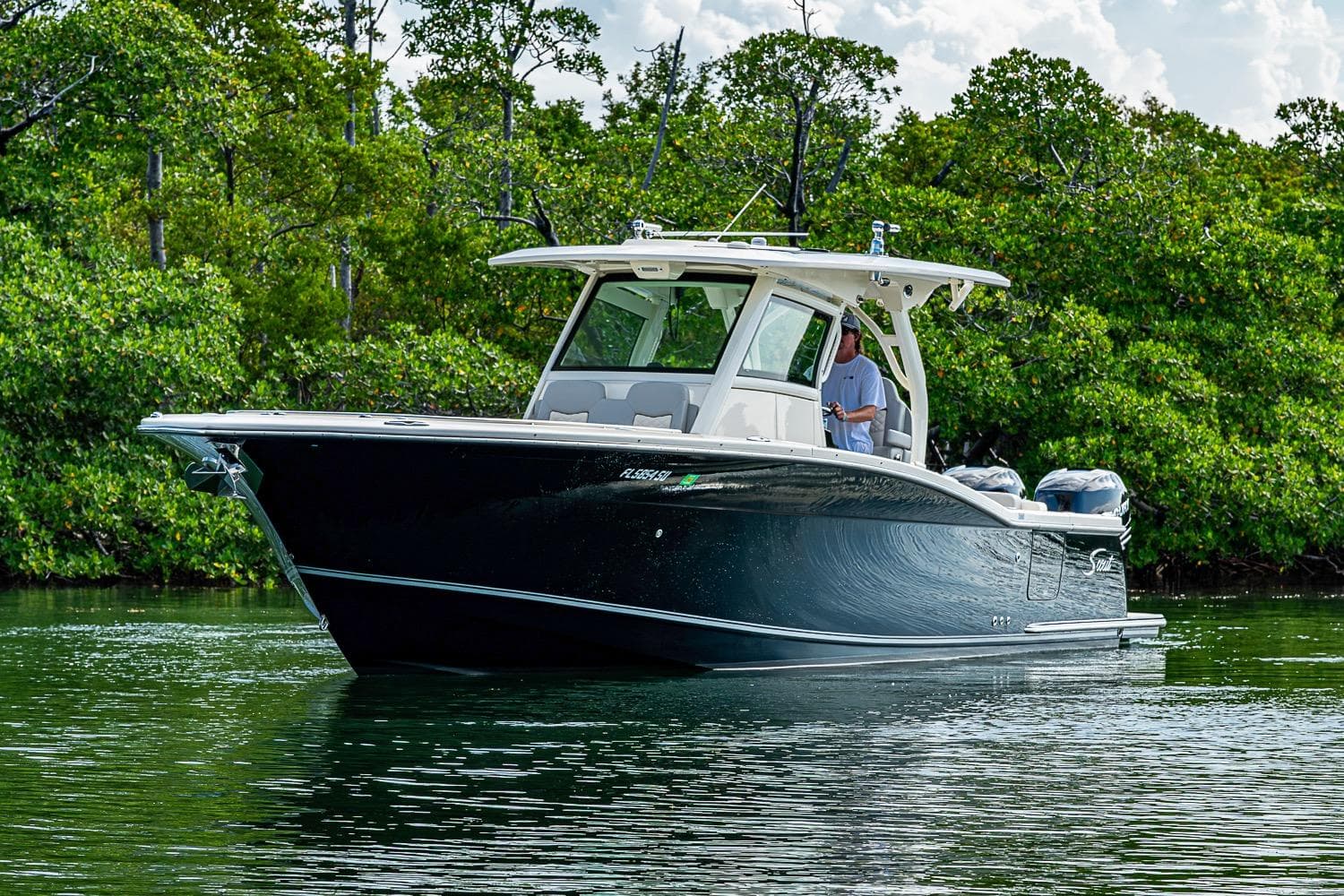 2021 Scout 330 LXF boat cruising on calm water near lush greenery.