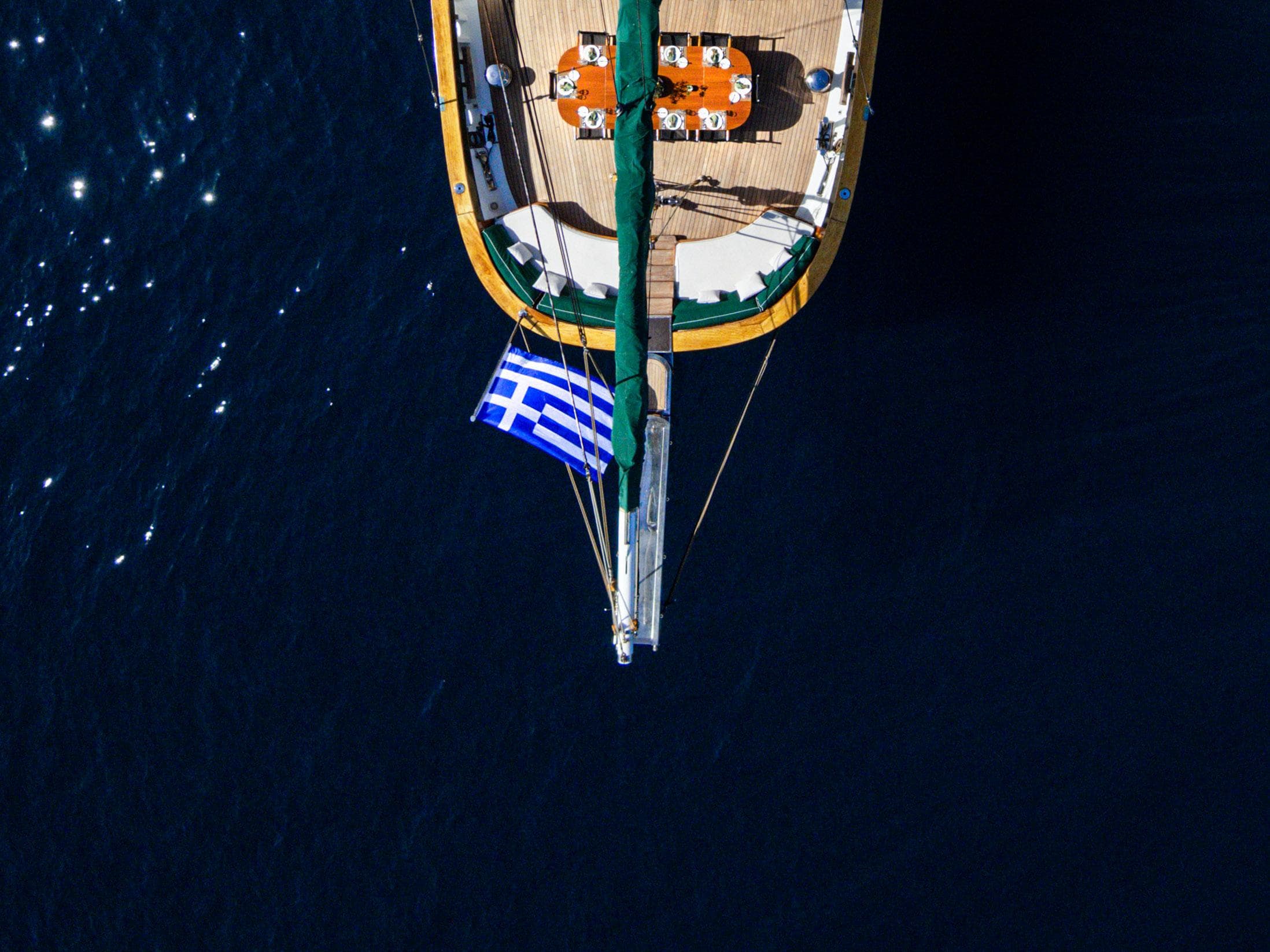 Aerial view of a custom 2004 sailboat with Greek flag on deep blue sea.