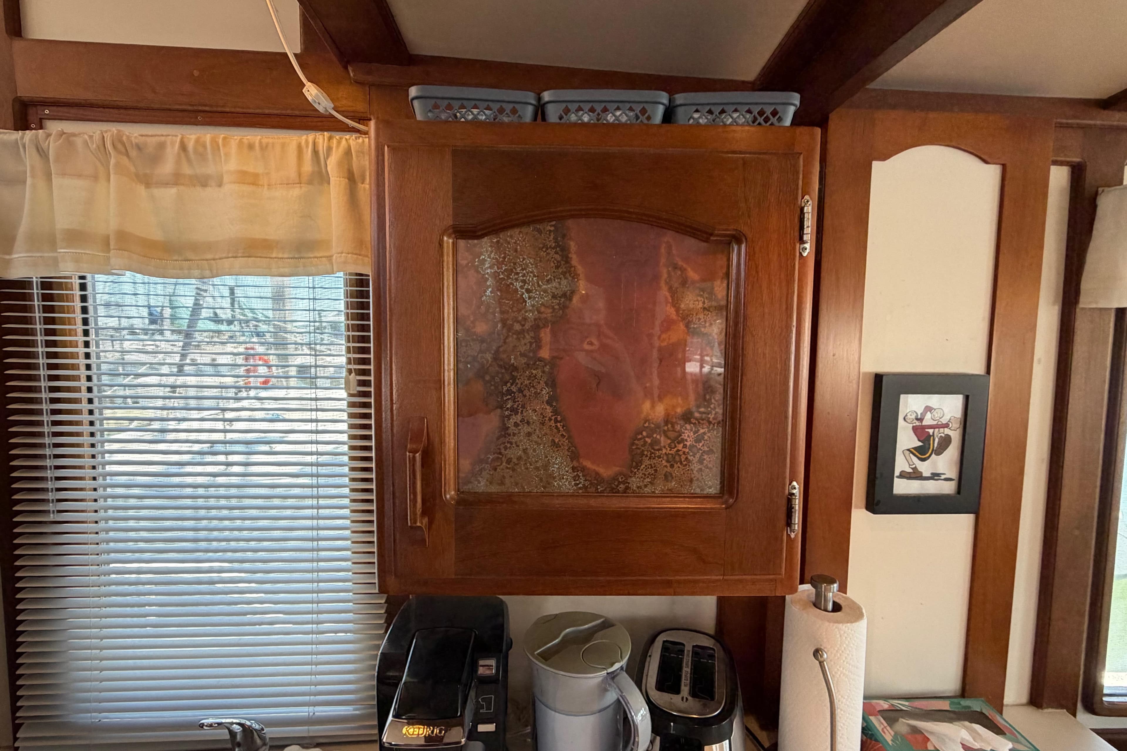 Wooden cabinet with glass door in a cozy kitchen, featuring a coffee maker and toaster.