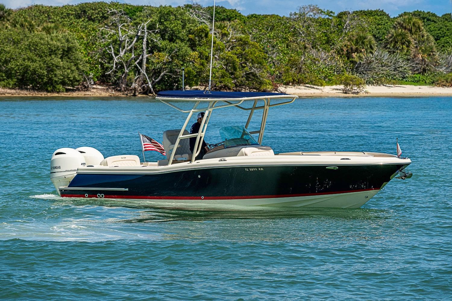 2017 Chris-Craft Catalina 26 boat cruising on blue water near a lush shoreline.
